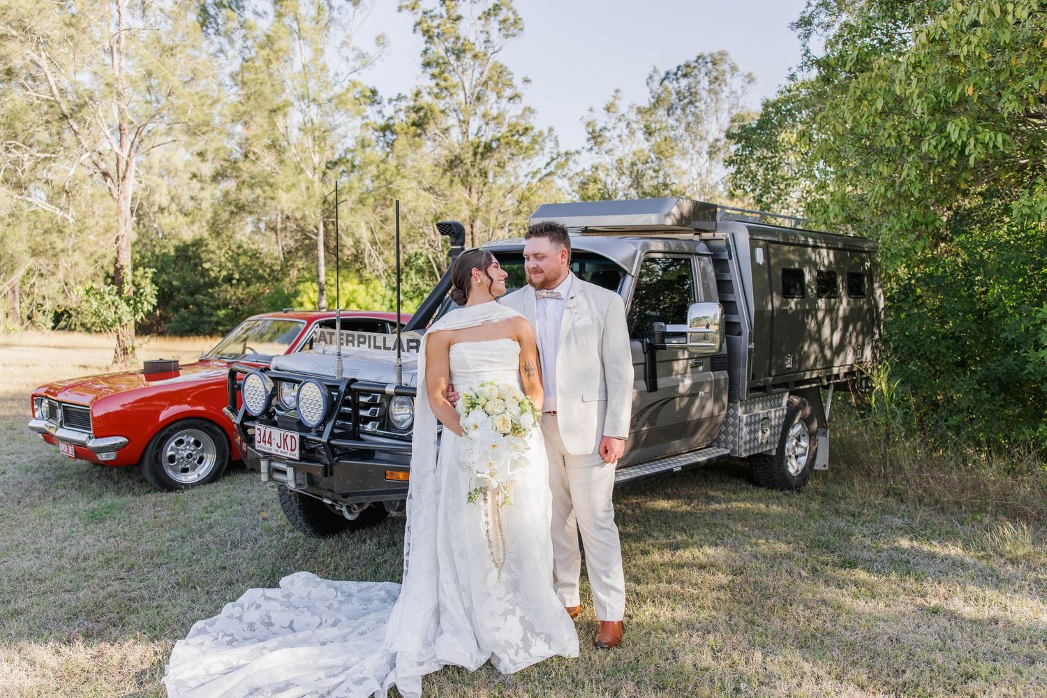 Vintage cars parked in a rustic outdoor wedding setting among trees.