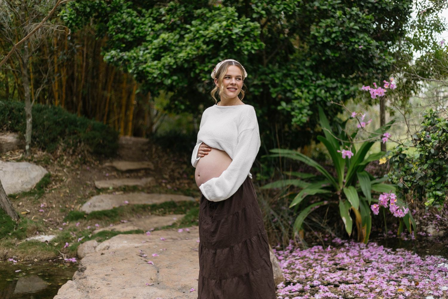 Romantic garden photoshoot with lush greenery and purple flowers in background.