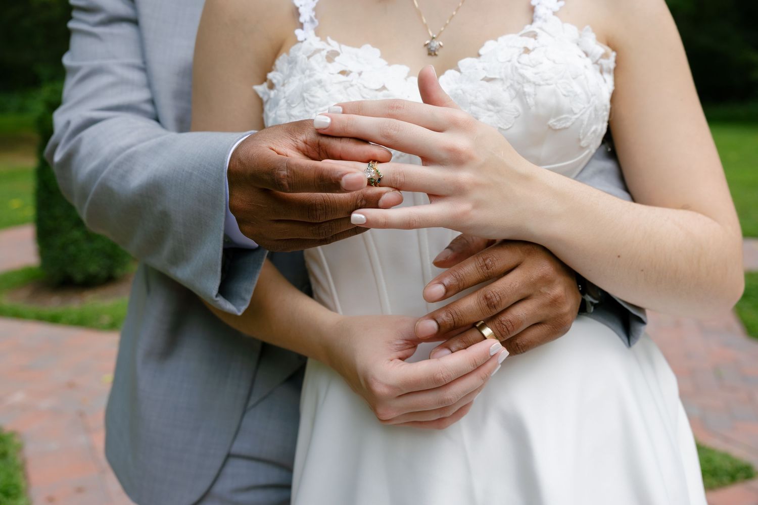 Newlywed couple displaying gold wedding rings, bride in white lace dress, groom in gray suit.