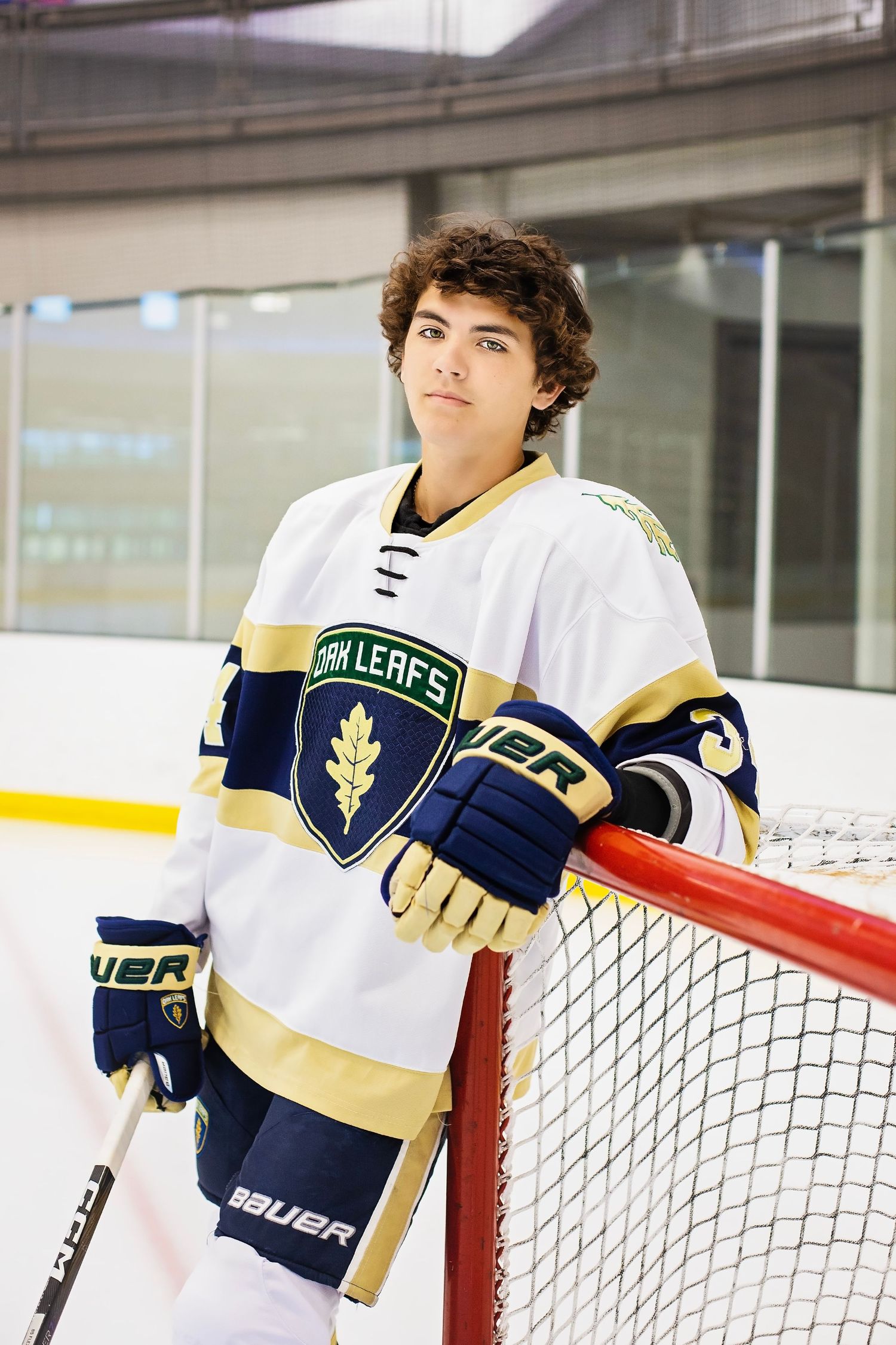 Teen hockey player in Oak Leafs jersey leans against goal post on indoor ice rink.