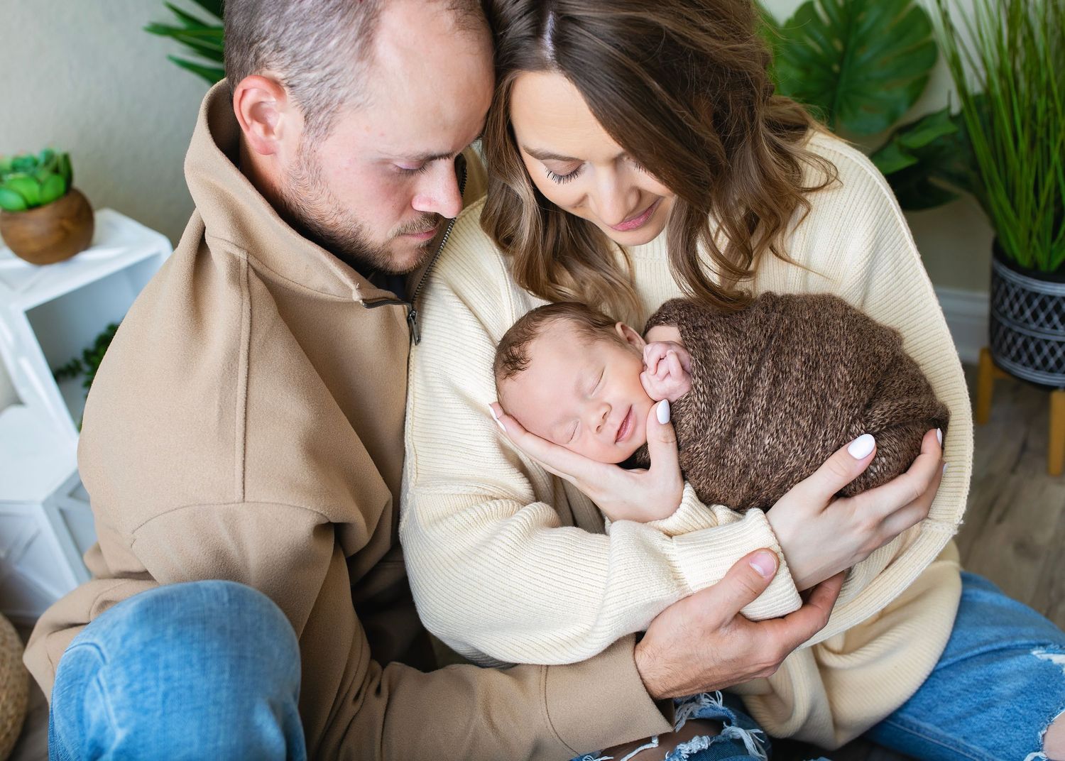 New parents tenderly gaze at their sleeping newborn wrapped in brown swaddle cloth.