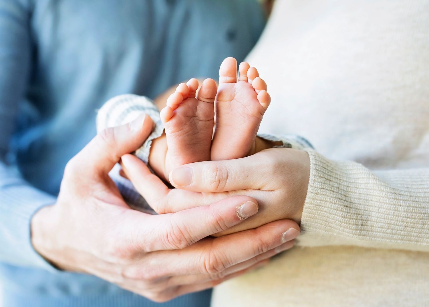 Parents cradling tiny newborn baby feet in their hands, close-up lifestyle newborn photography.