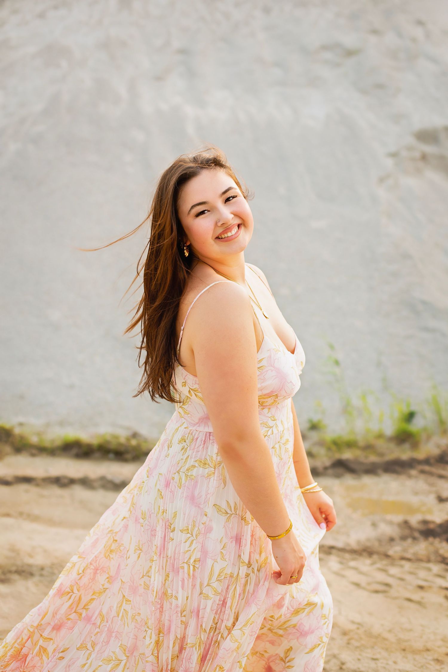 Smiling young woman in pink floral dress with wind-blown hair outdoors.