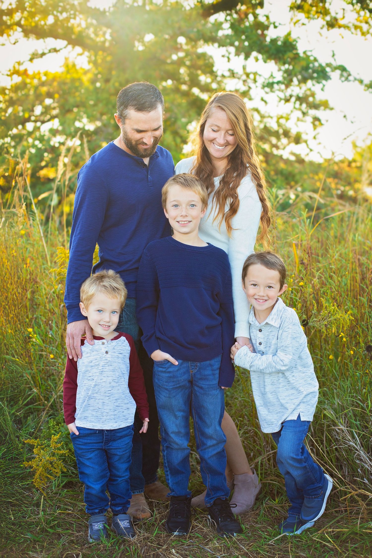 Family of five standing together in a sunny meadow with wildflowers at golden hour.