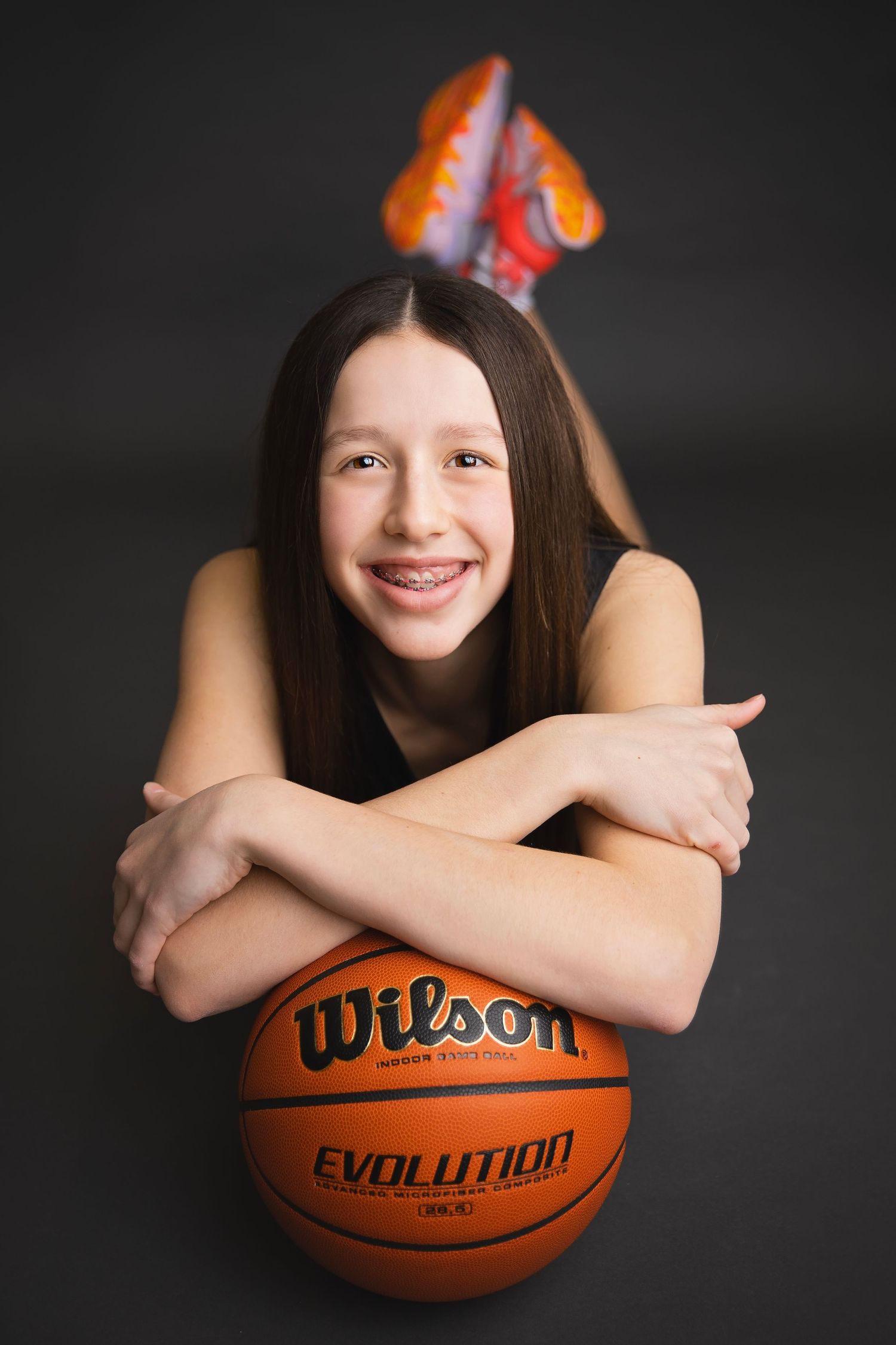 Smiling girl with braces poses with a Wilson Evolution basketball on a dark background.