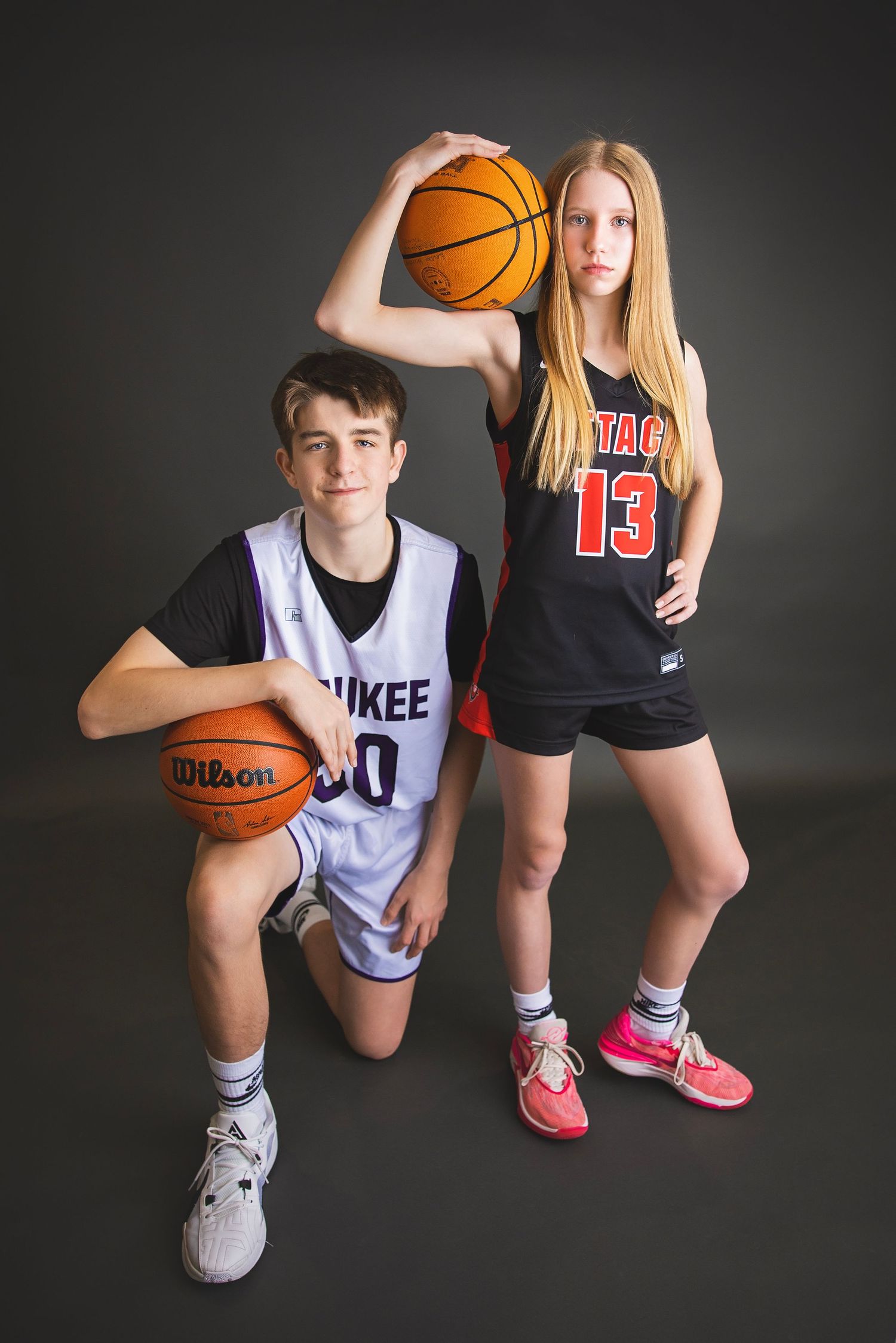 Teen boy and girl in basketball uniforms posing with basketballs.