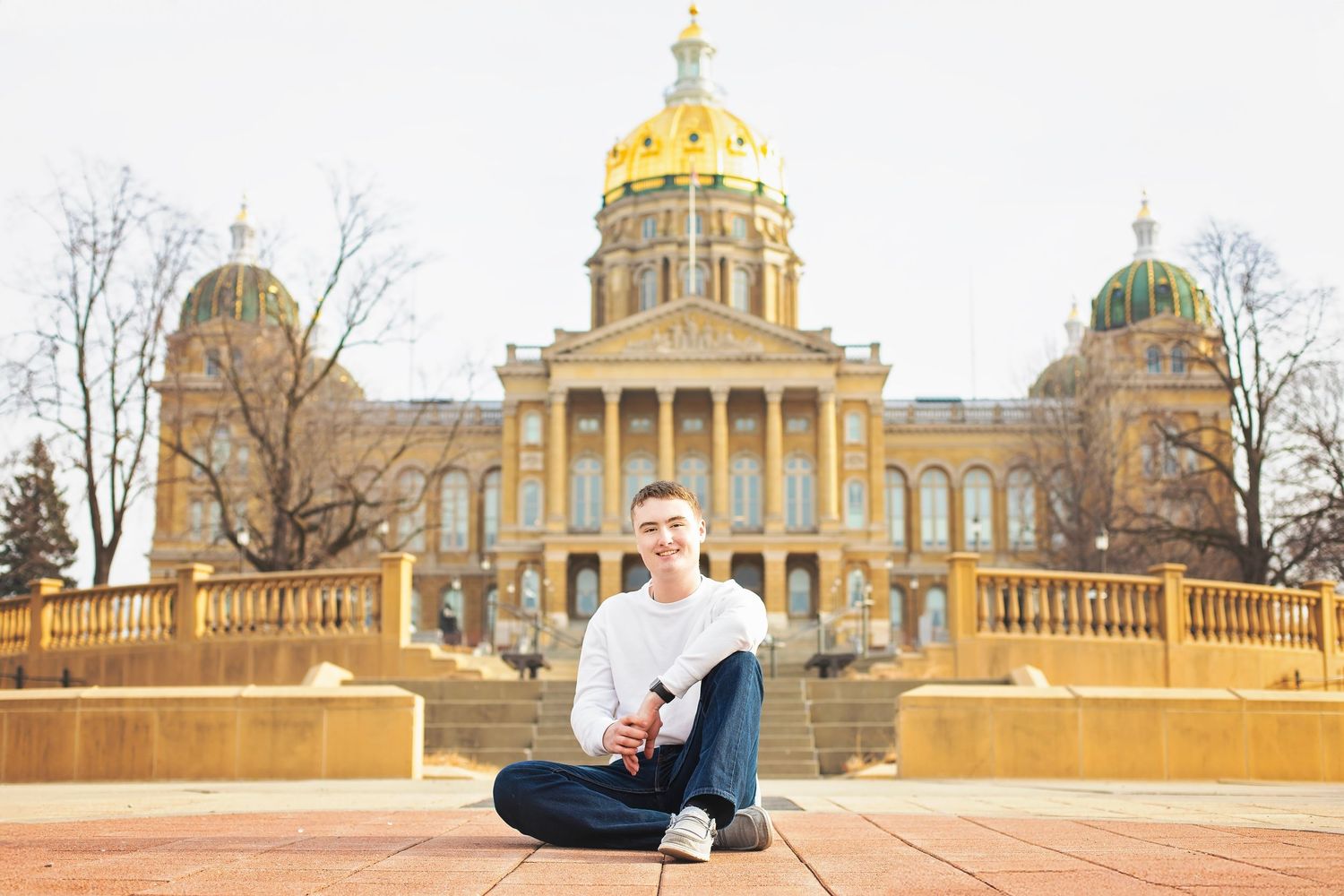 Young man sitting cross-legged on plaza in front of Iowa State Capitol building.