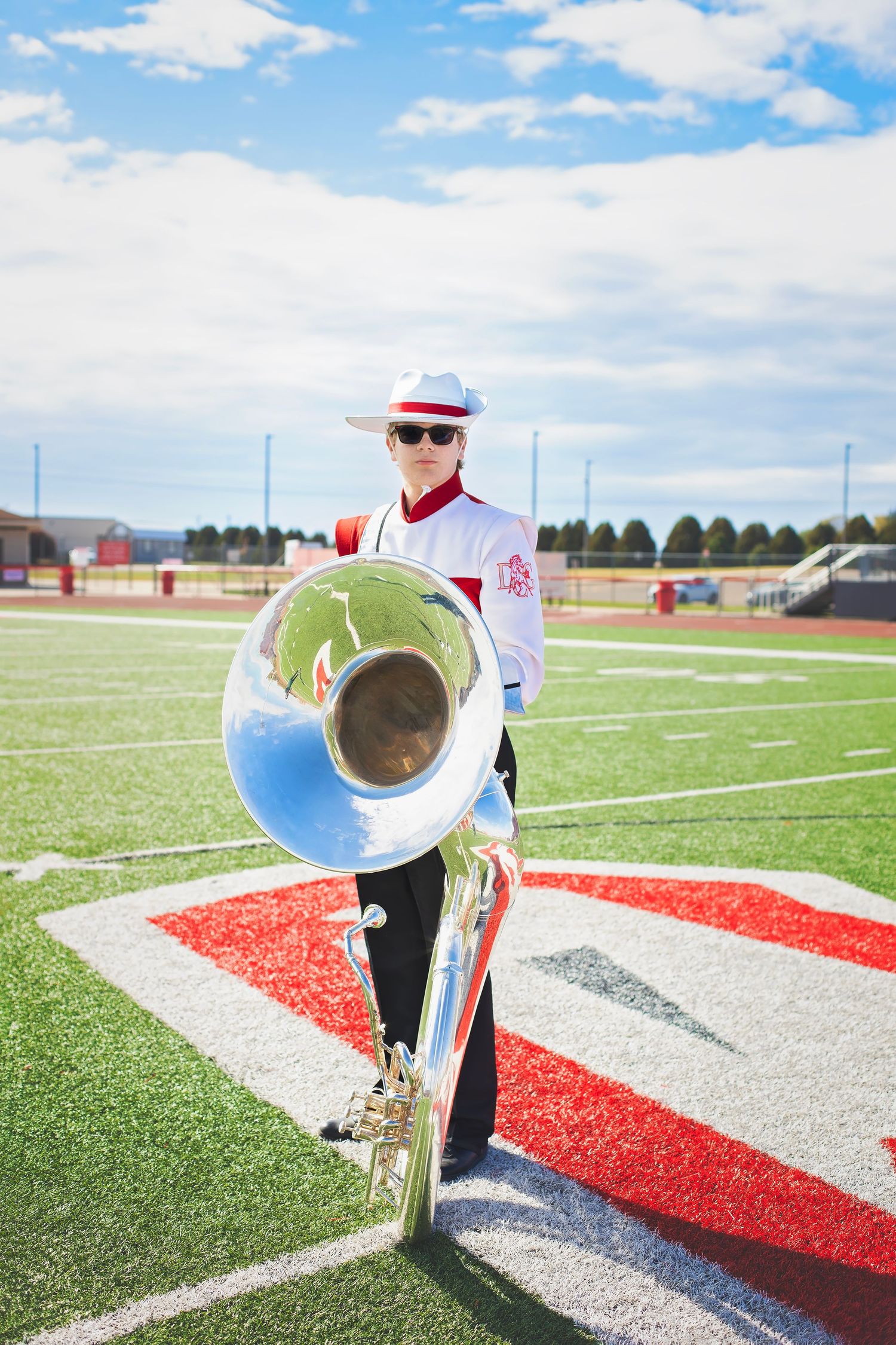 Marching band member in red and white uniform holding a sousaphone on a football field.