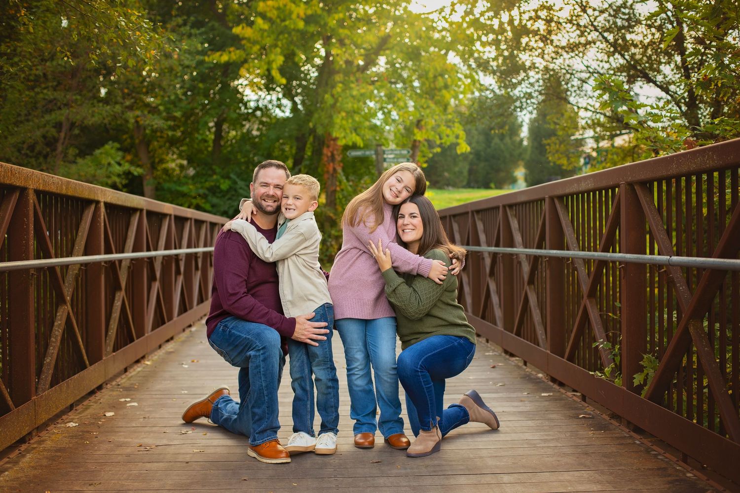 A happy family of four poses together on a wooden bridge in fall foliage.