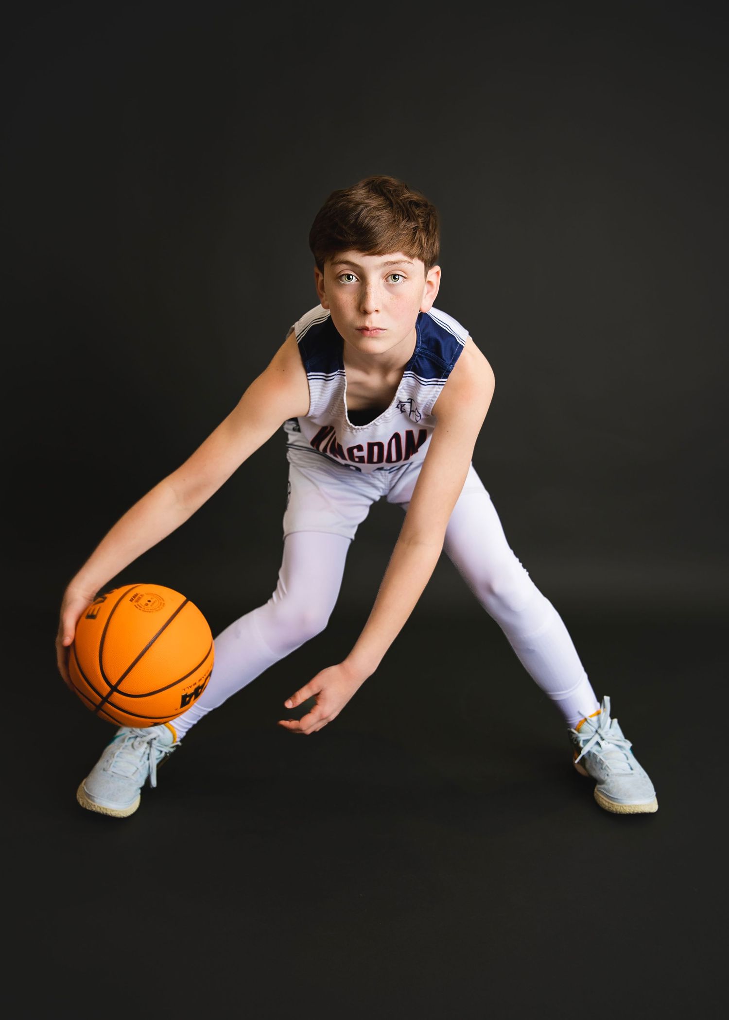 Young boy in Kingdom Hoops jersey dribbling a basketball in a wide stance pose.