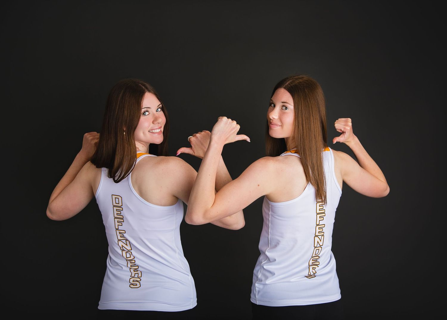 Two young women in white tank tops flex their muscles back-to-back in a fun sports photo.