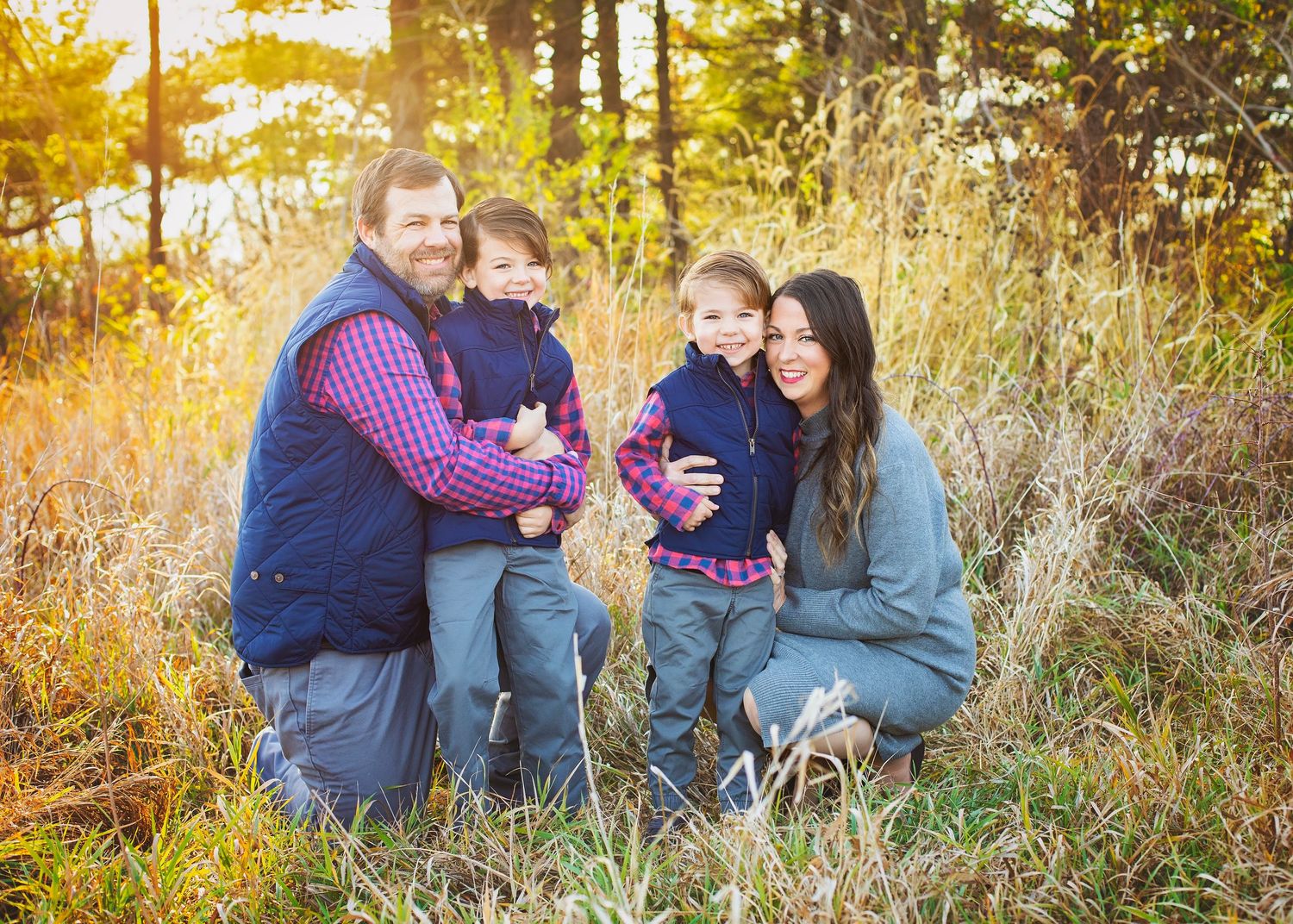 A smiling family of four poses together in a golden autumn meadow during a warm outdoor family portrait.