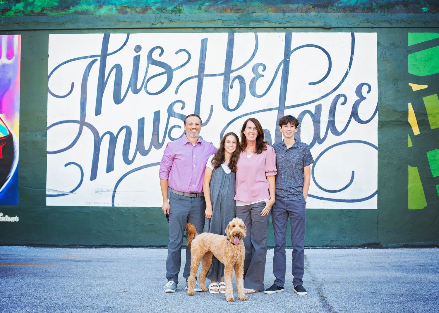 Family of four with a golden doodle posing in front of a colorful mural.