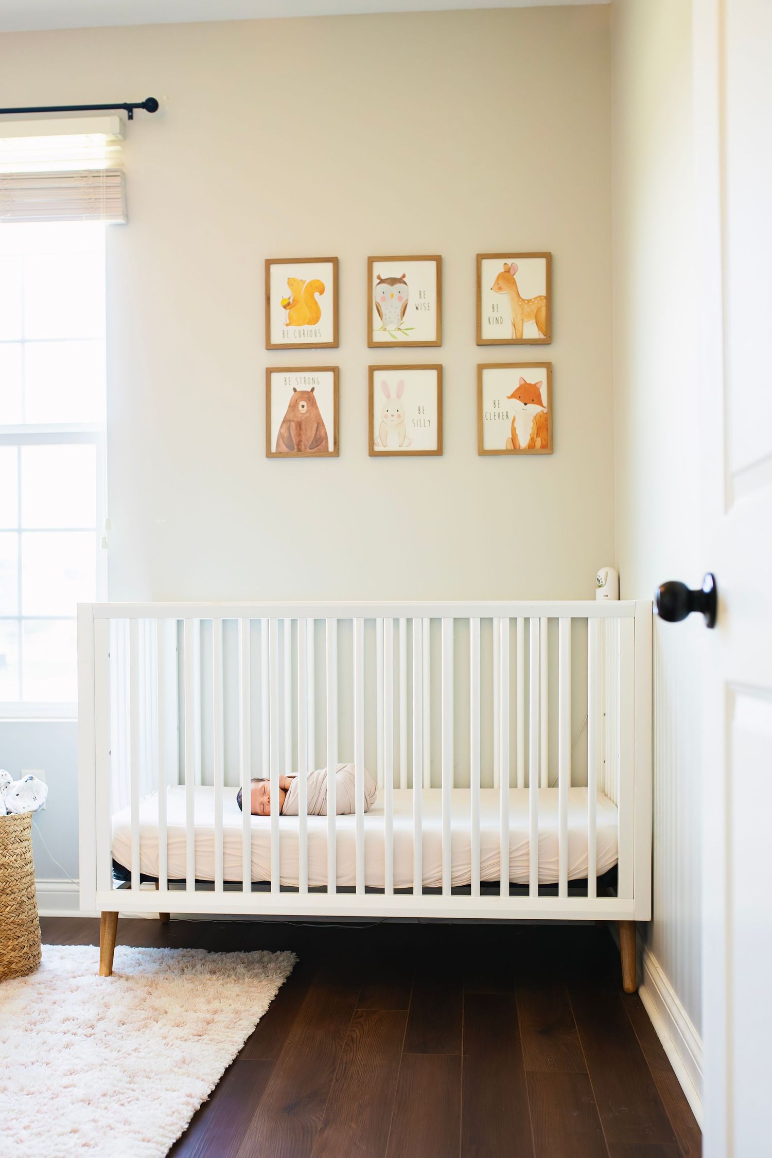 White modern nursery crib with woodland animal wall art prints in a bright, clean baby room.