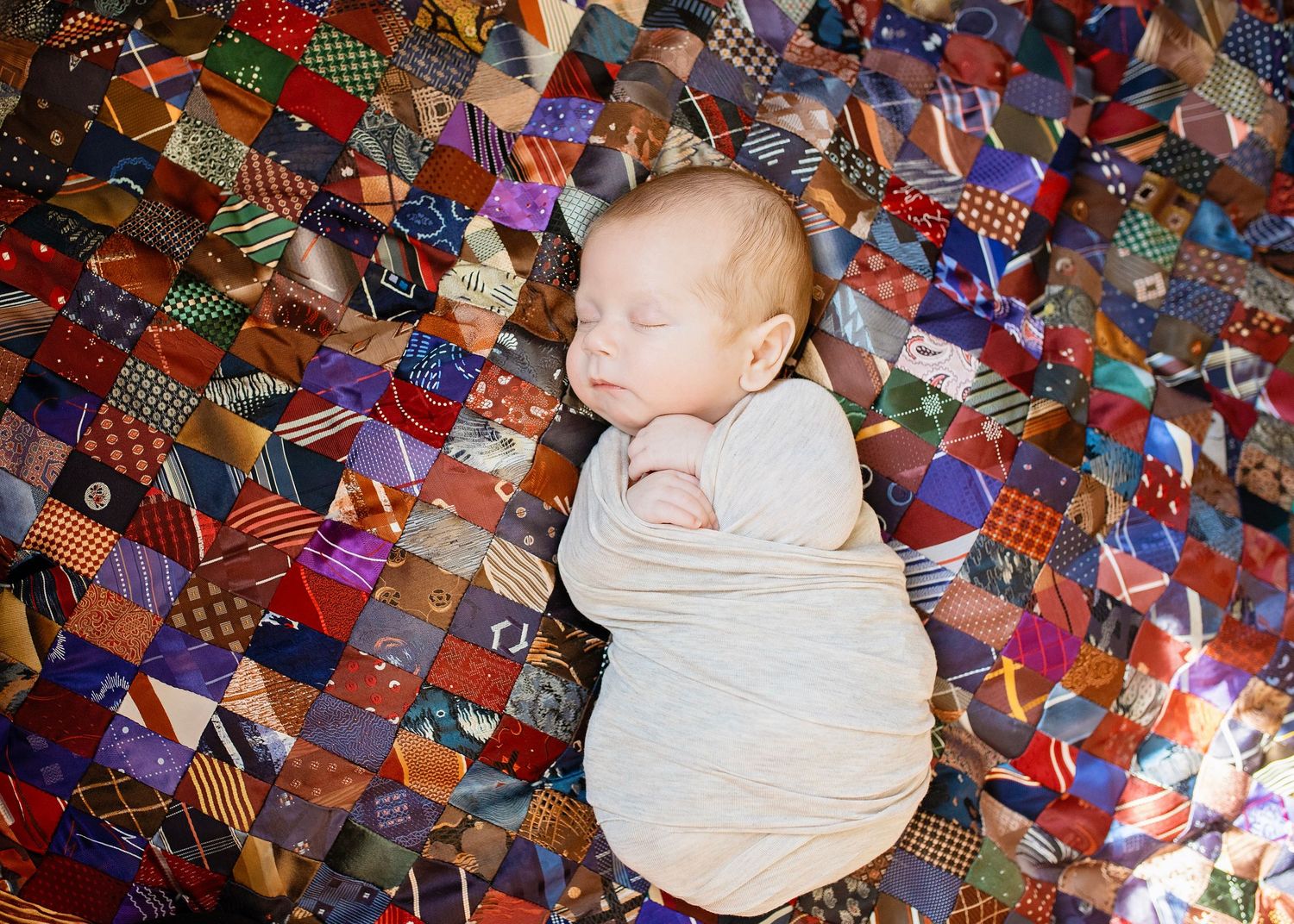 Peaceful newborn baby sleeping on a colorful patchwork quilt made of various fabric patterns.