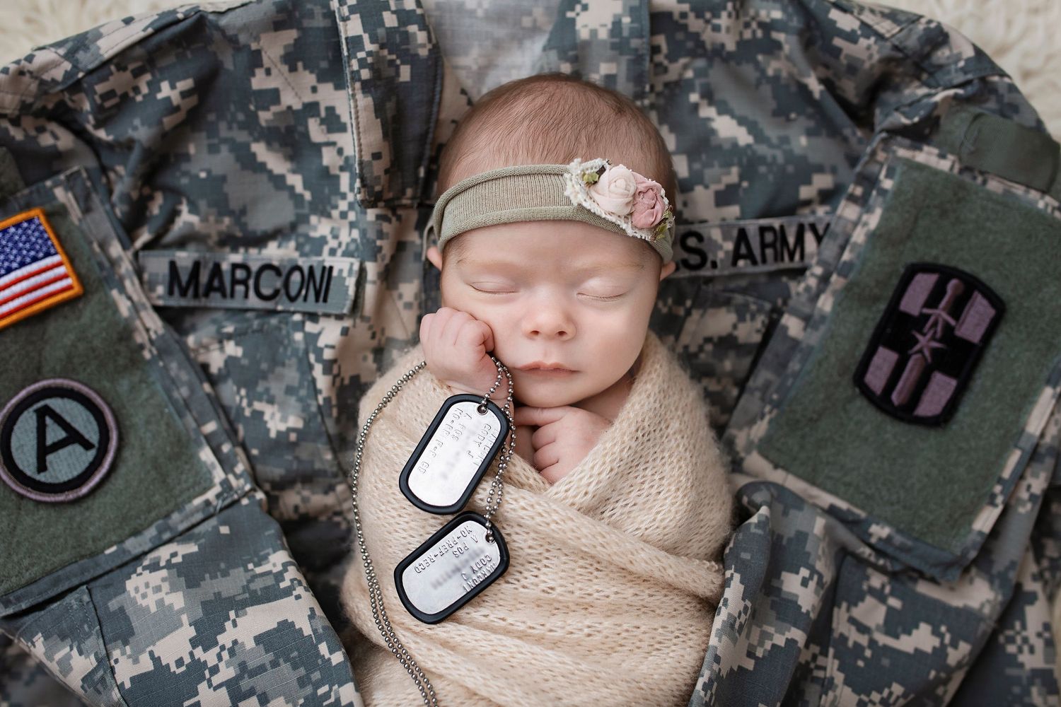 Newborn baby swaddled in beige wrap sleeping on US Army military uniform with dog tags.