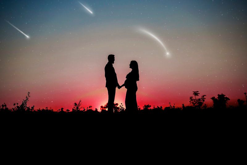 Romantic silhouette couple holding hands under shooting stars at red sunset sky.