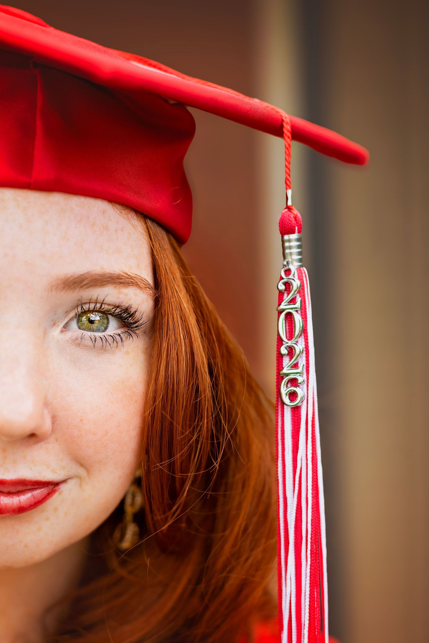 A young redhead woman wearing a red graduation cap with a 2026 tassel, posing for a senior portrait photo.
