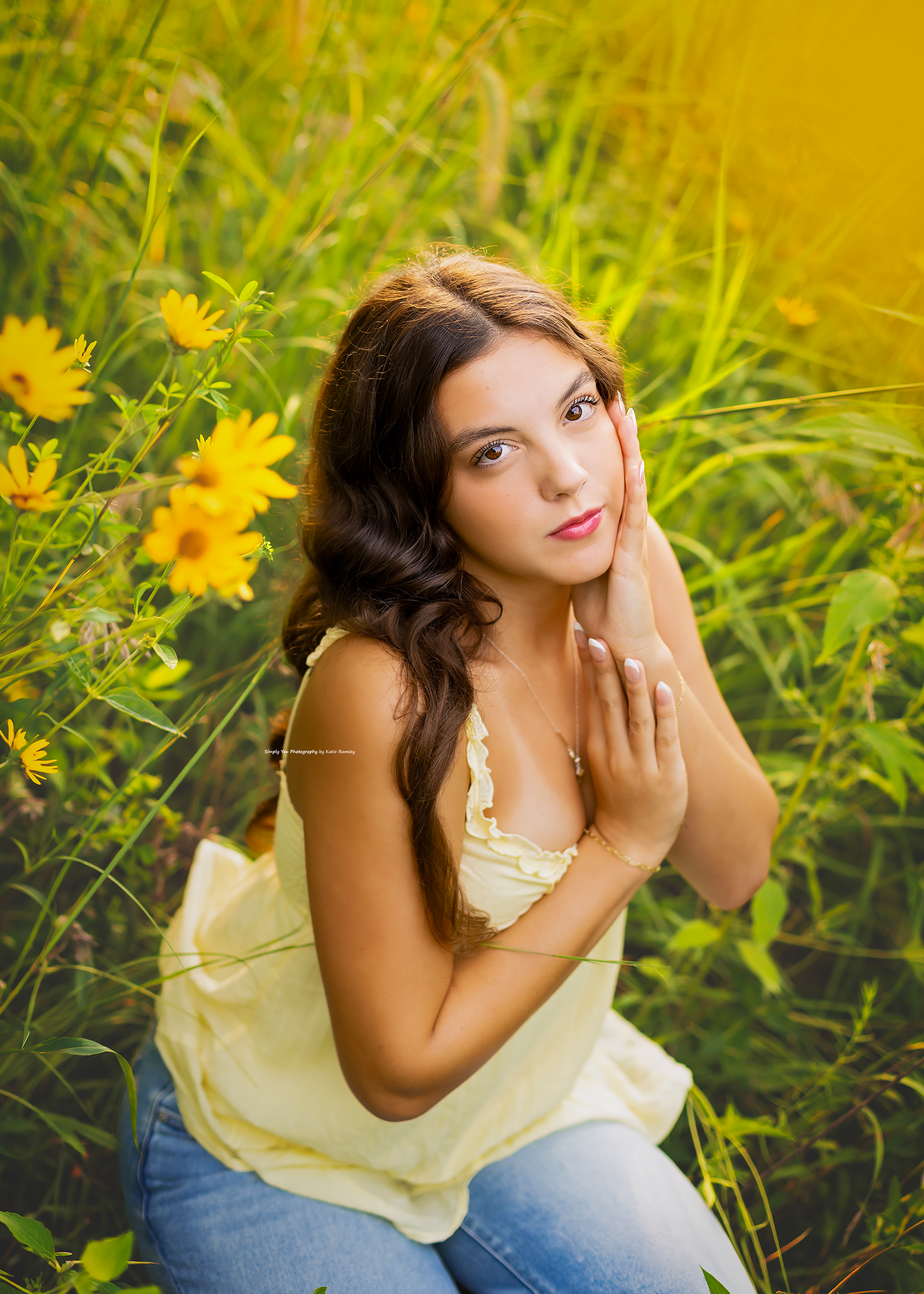 Young woman in yellow top sitting among vibrant yellow wildflowers in a lush green field, posing gracefully.