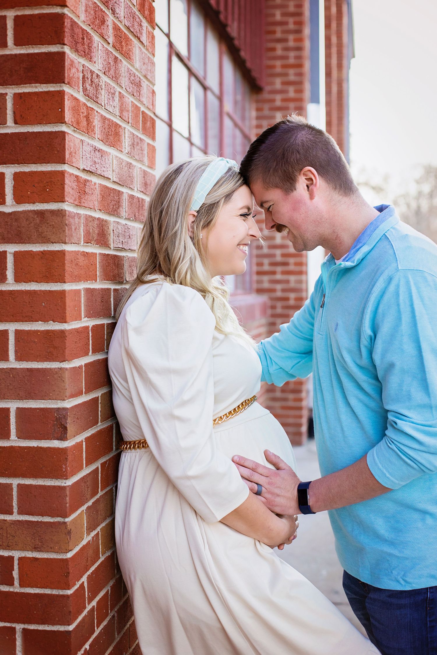 Expecting couple sharing an intimate forehead touch against a red brick wall.