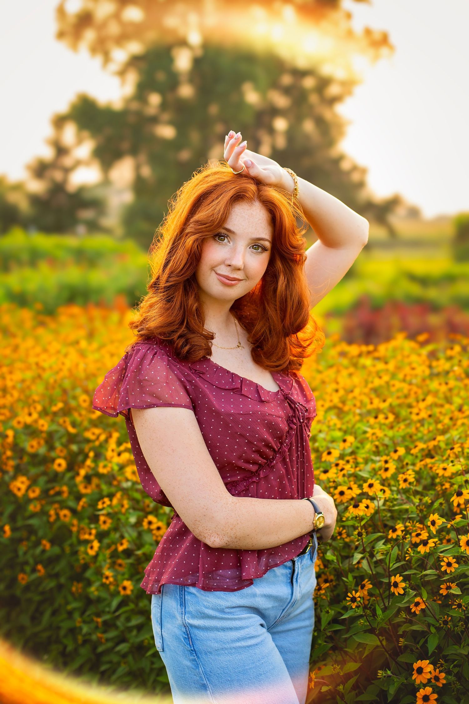 Redhead girl in maroon top posing in a field of yellow flowers at golden hour.