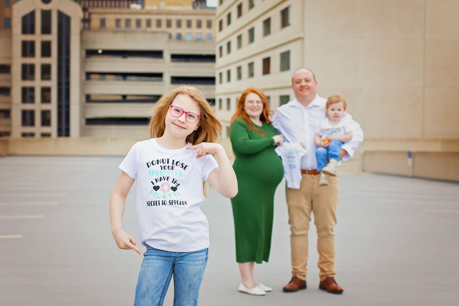 Family photo with redheaded girl in foreground and parents with baby behind her.