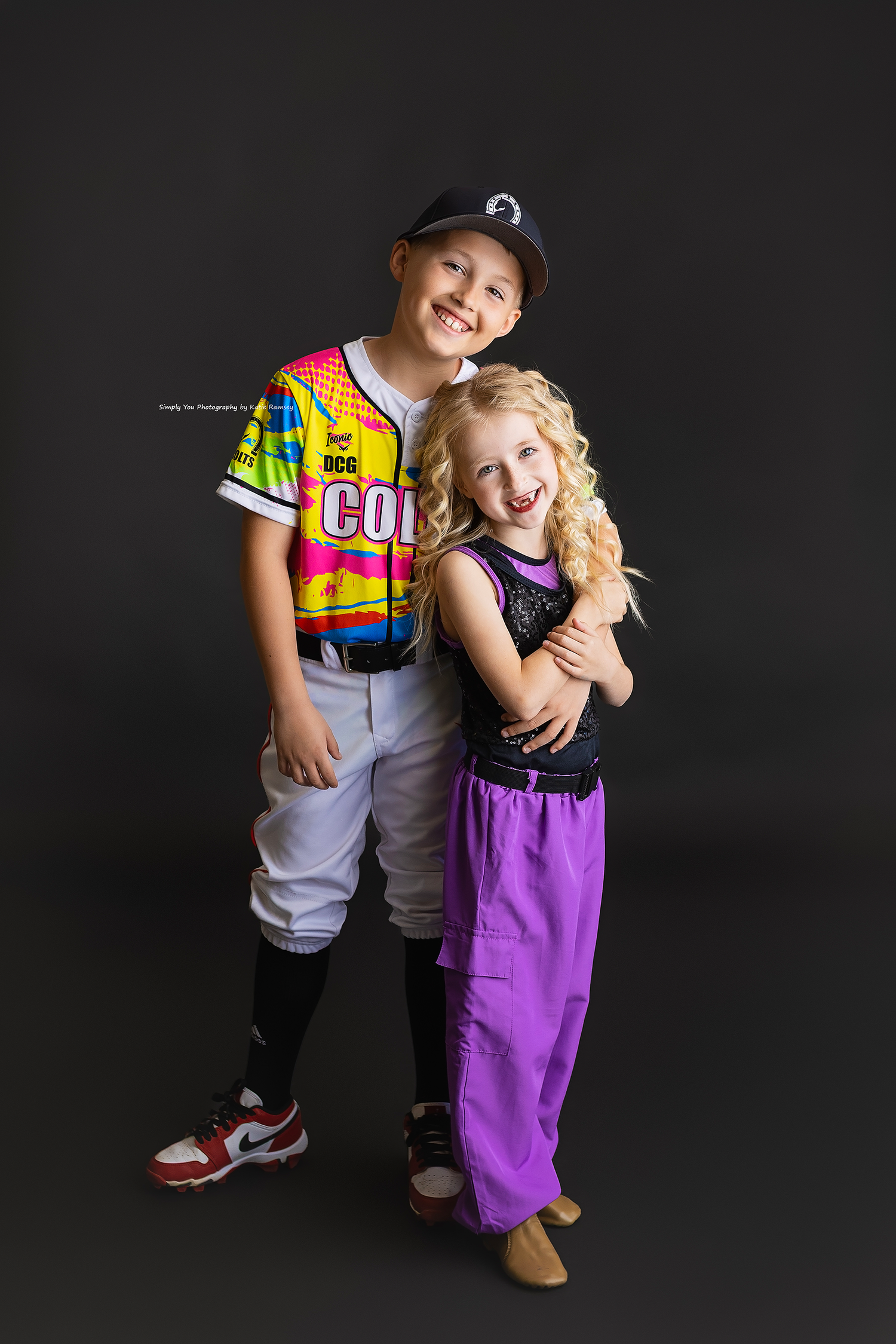 Smiling boy in Colts baseball uniform poses with blonde girl in purple pants and black sequin top.