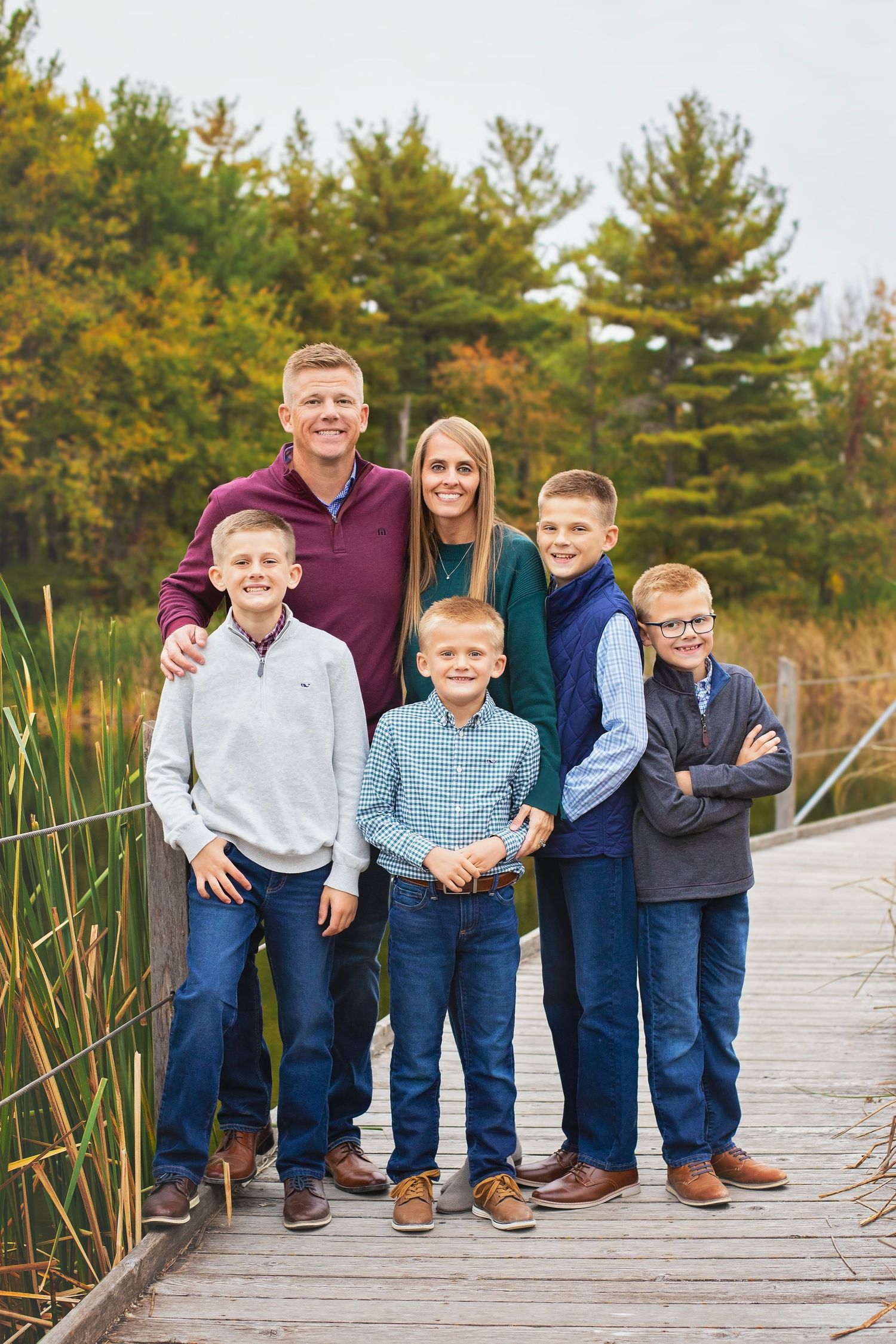Family of six posing on a wooden boardwalk surrounded by autumn wetlands.