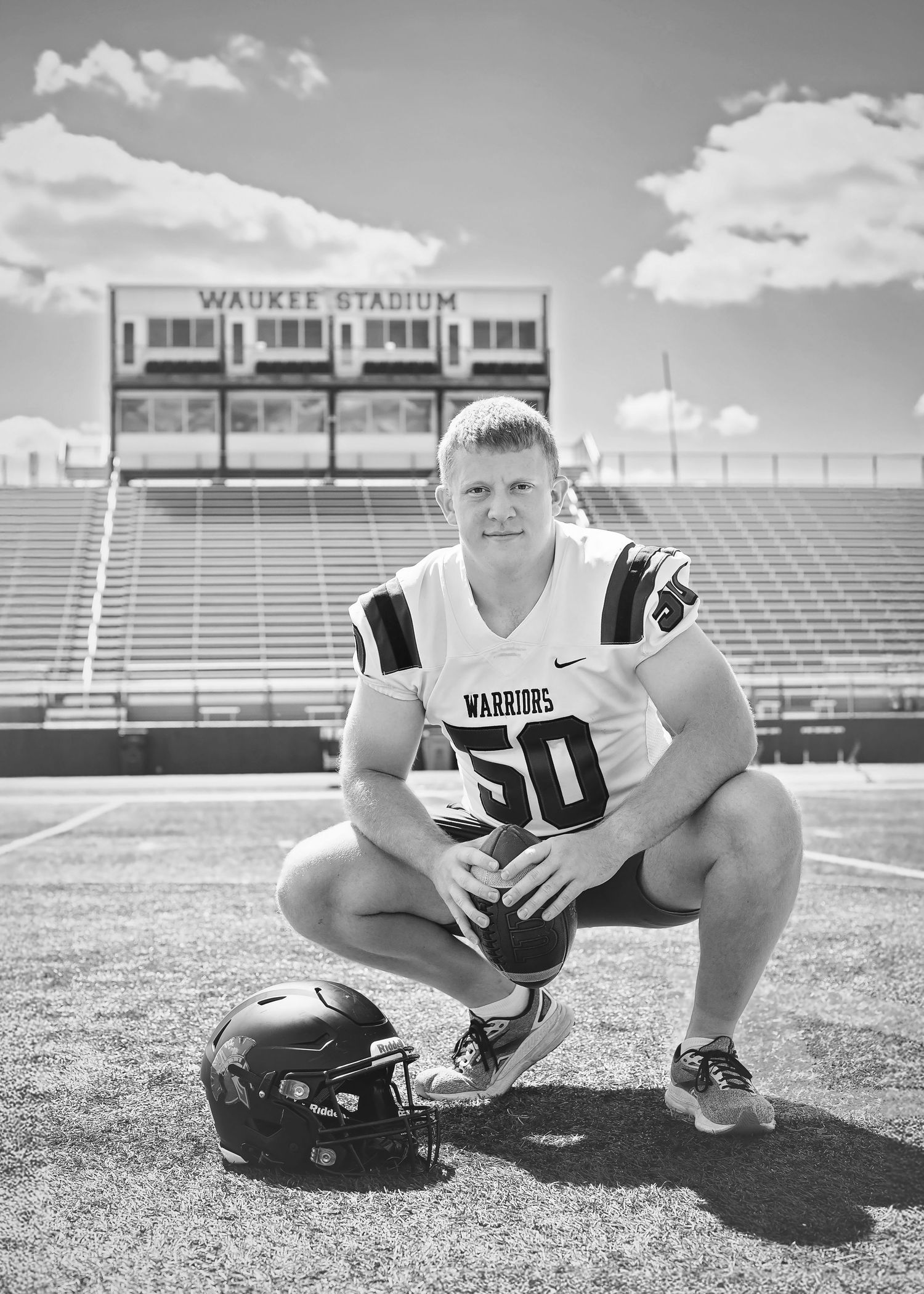 Black and white photo of football player number 50 kneeling at Waukee Stadium field.