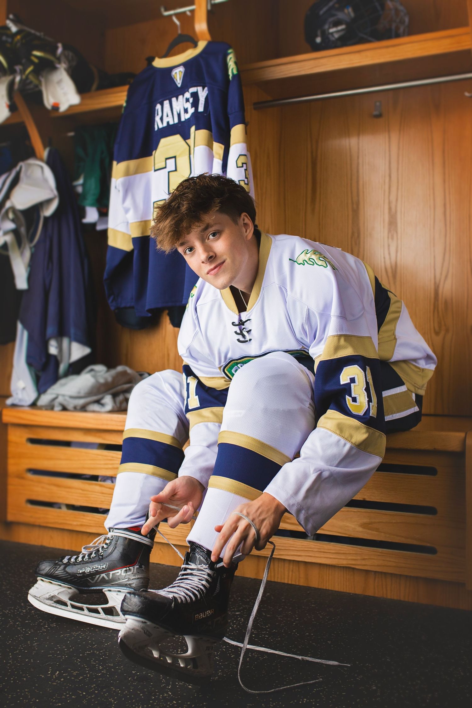 Teen hockey player in Oak Leafs jersey number 31 lacing skates in locker room.