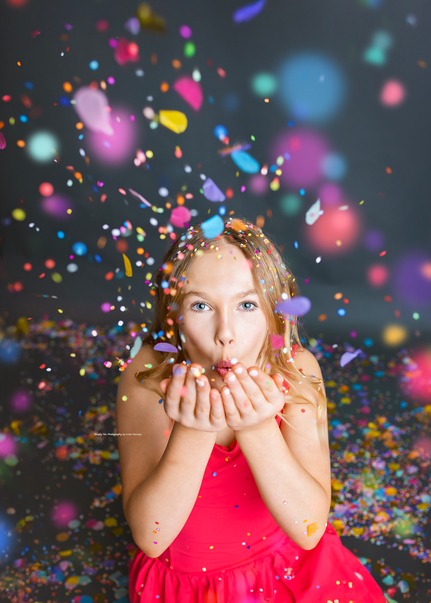 Young girl in a red dress blowing colorful confetti from her hands in a fun studio photo session.