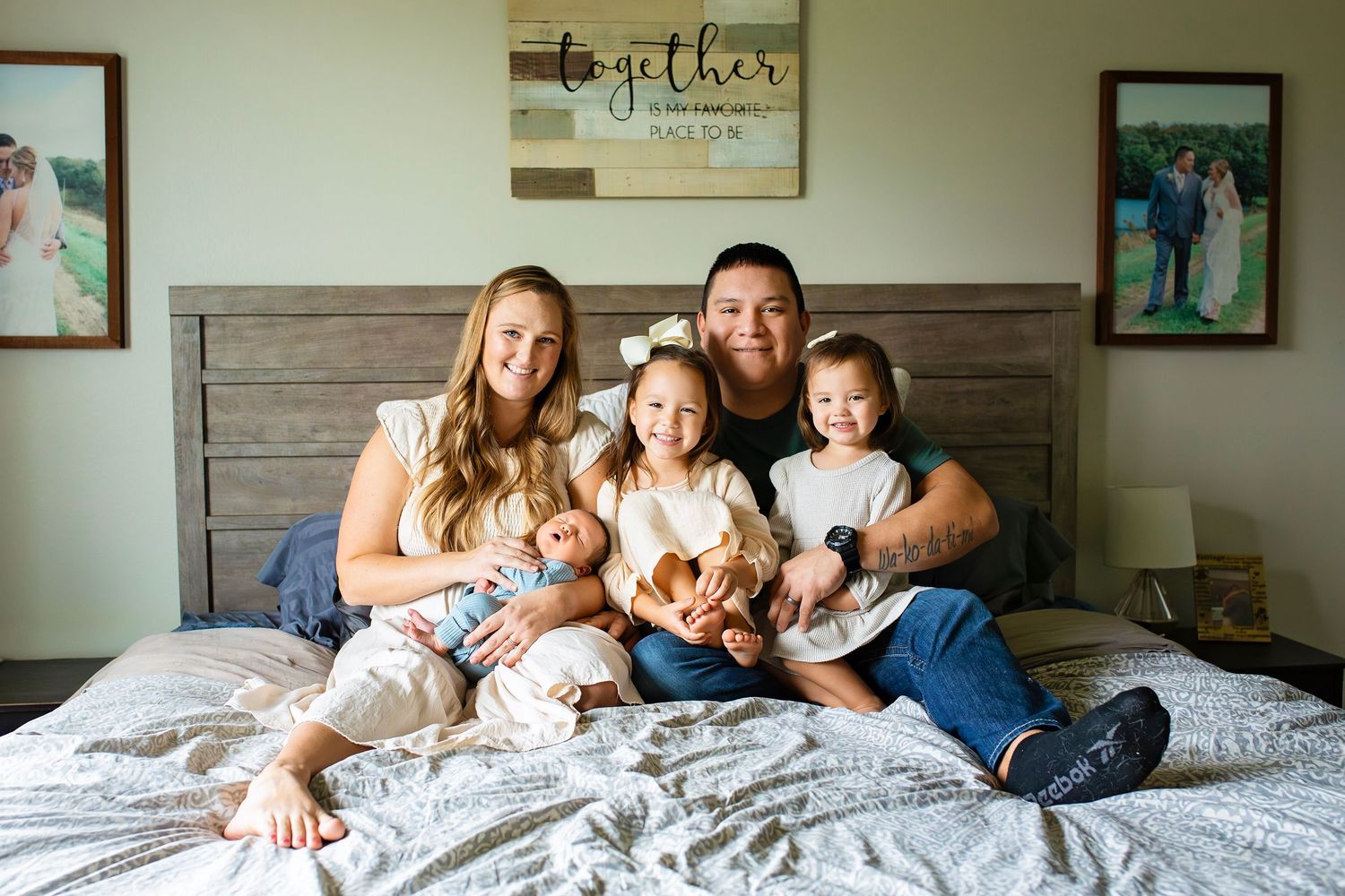 Happy family of five smiling together on a bed with a Together sign on the wall behind them.