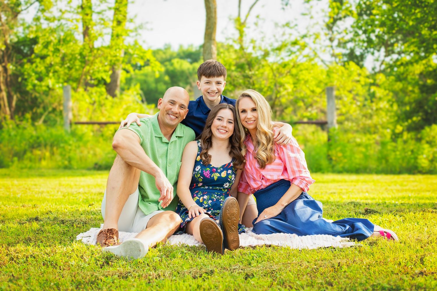 Happy family of four sitting together on blanket in lush green park during photo session.