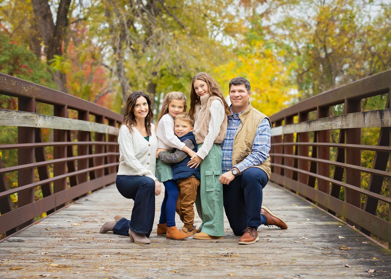 Family of five posing together on a wooden bridge surrounded by fall foliage.