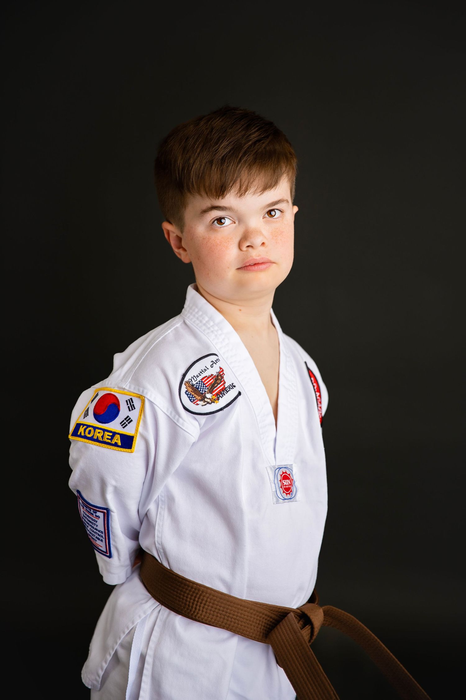 Young martial arts student in white gi with Korea patch and brown belt poses in studio.