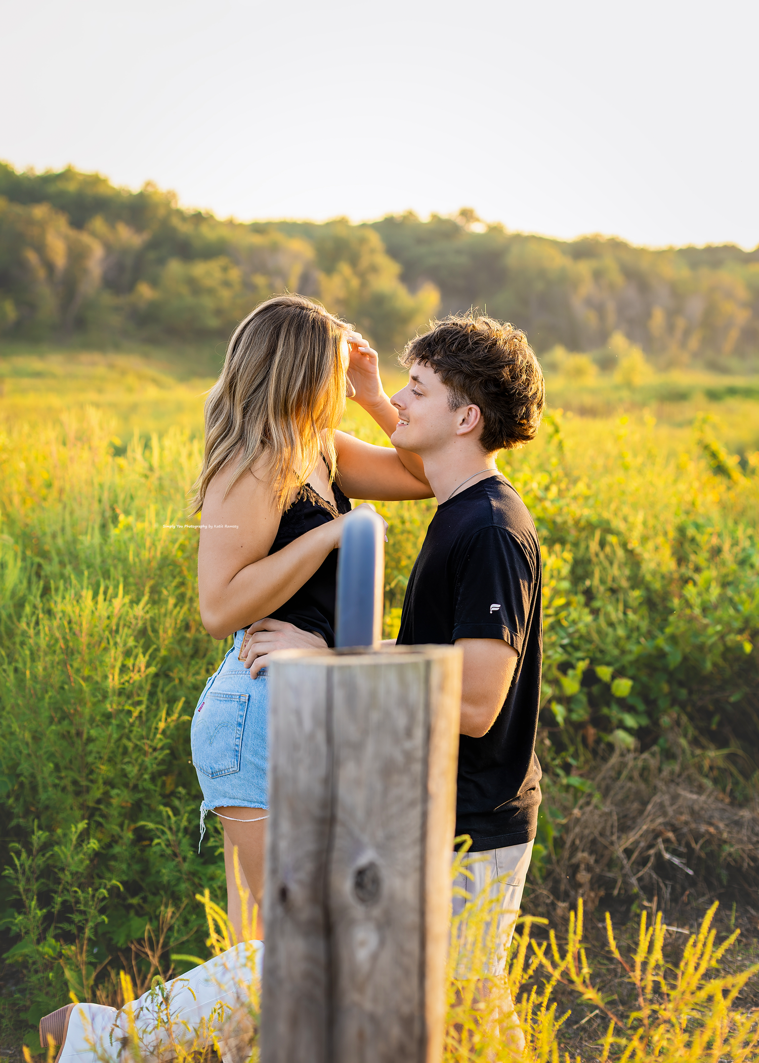 A young couple shares a romantic moment in a golden sunlit meadow, surrounded by lush green fields at sunset.