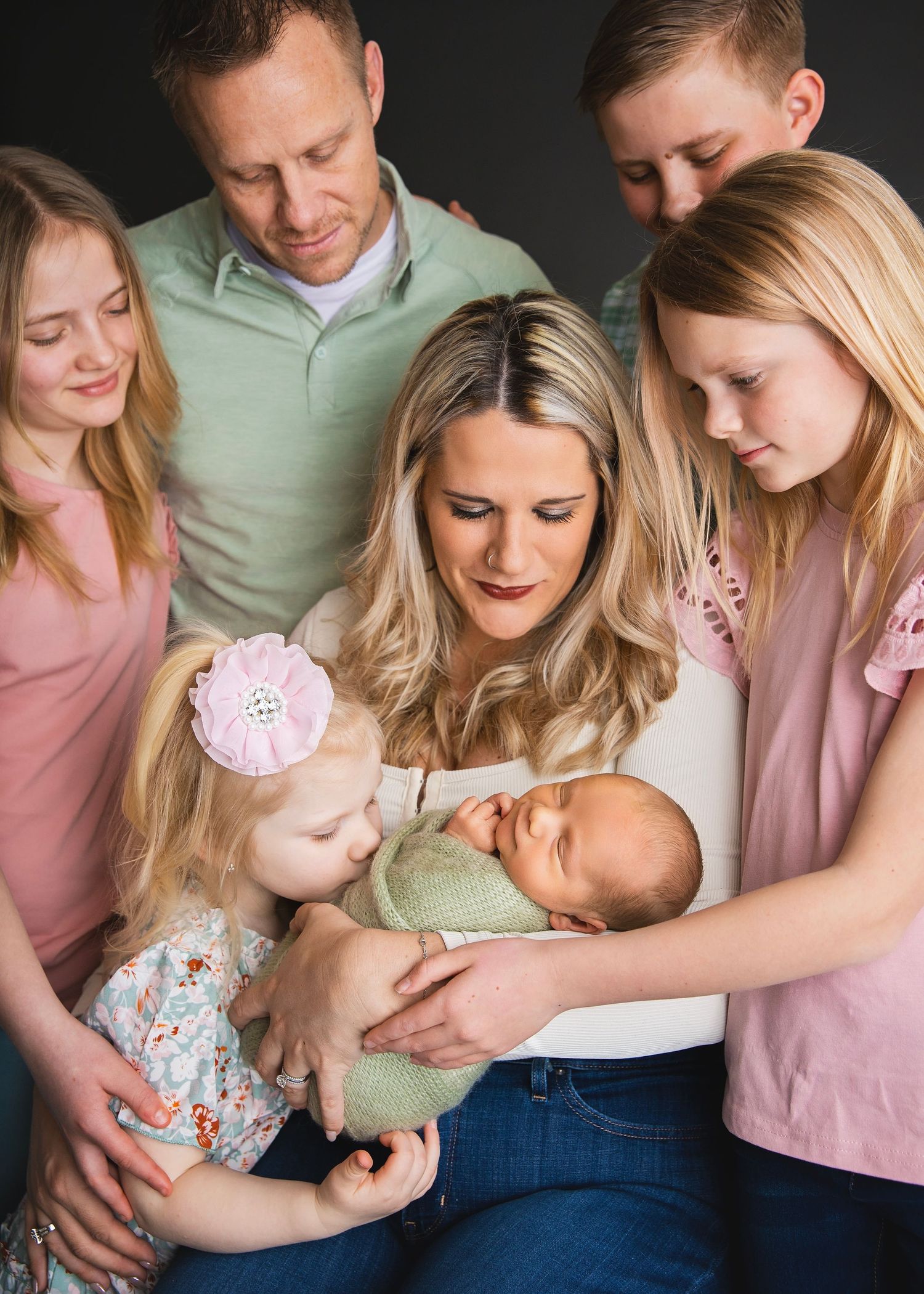 Large family gathered around a mother holding a newborn baby in a warm studio portrait.