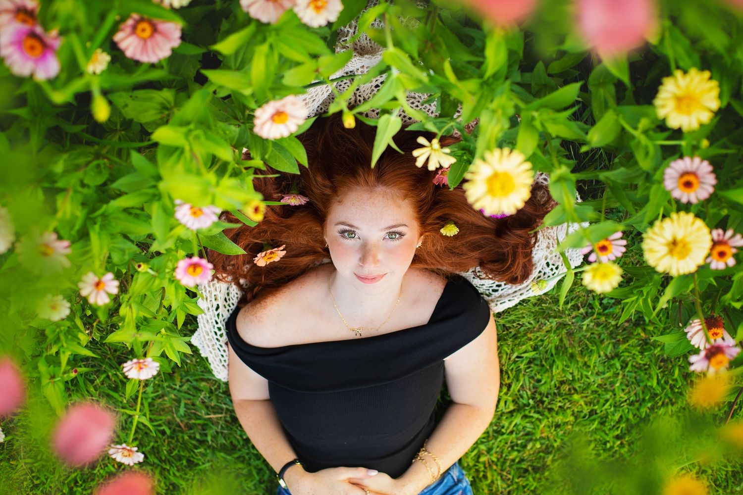 Aerial view of redhead girl lying in lush grass with colorful flowers around her.