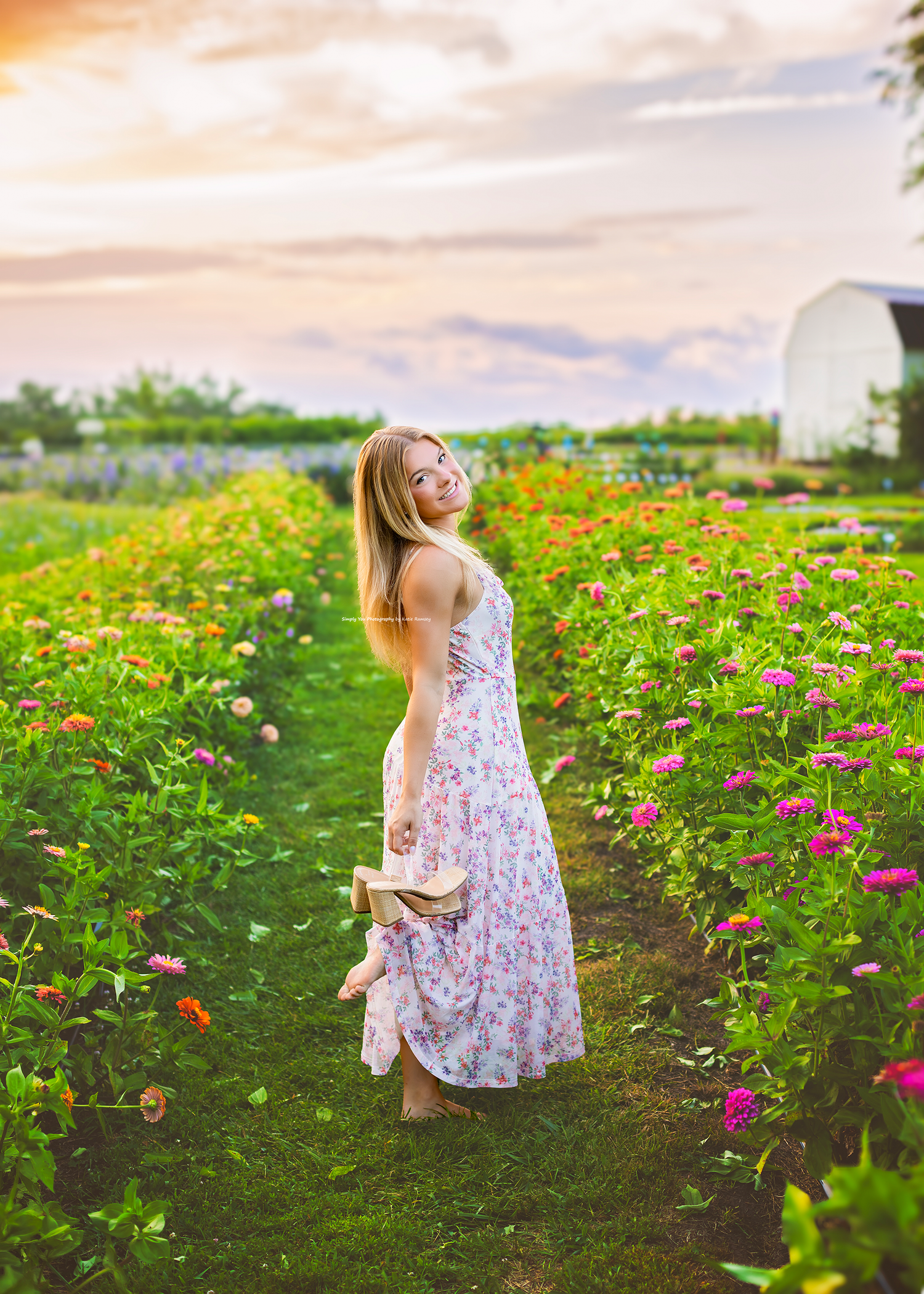 A blonde woman in a floral dress walks through a colorful flower farm at sunset.