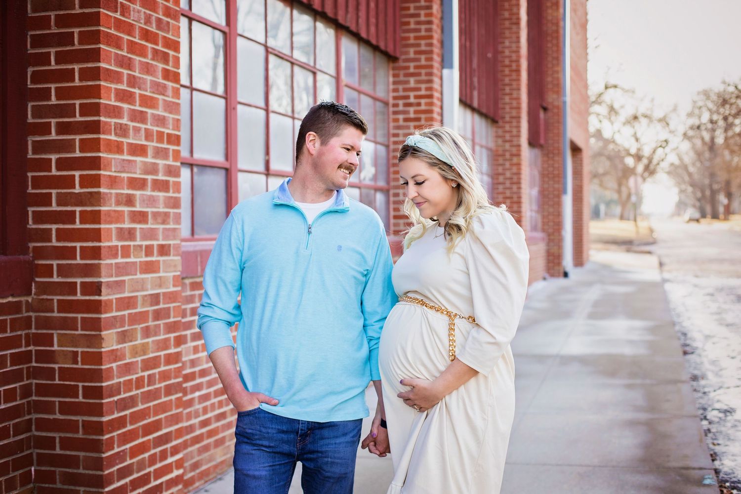 Couple sharing a tender moment during maternity photo shoot against a red brick building.