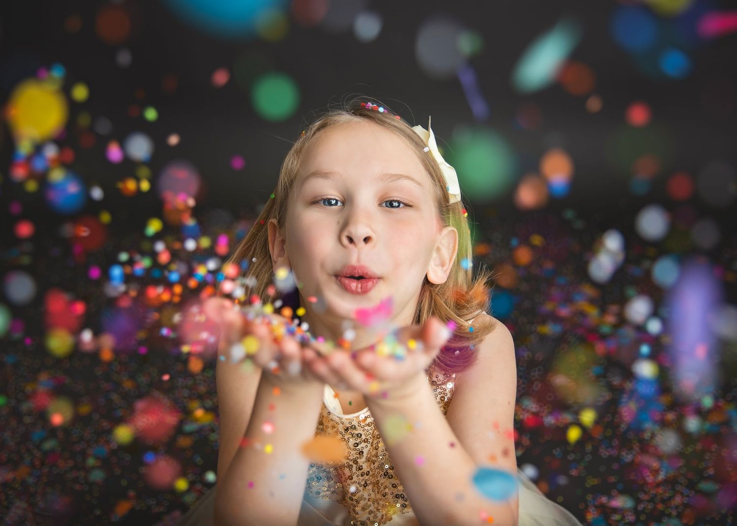 Young blonde girl blowing colorful confetti from her hands in studio.