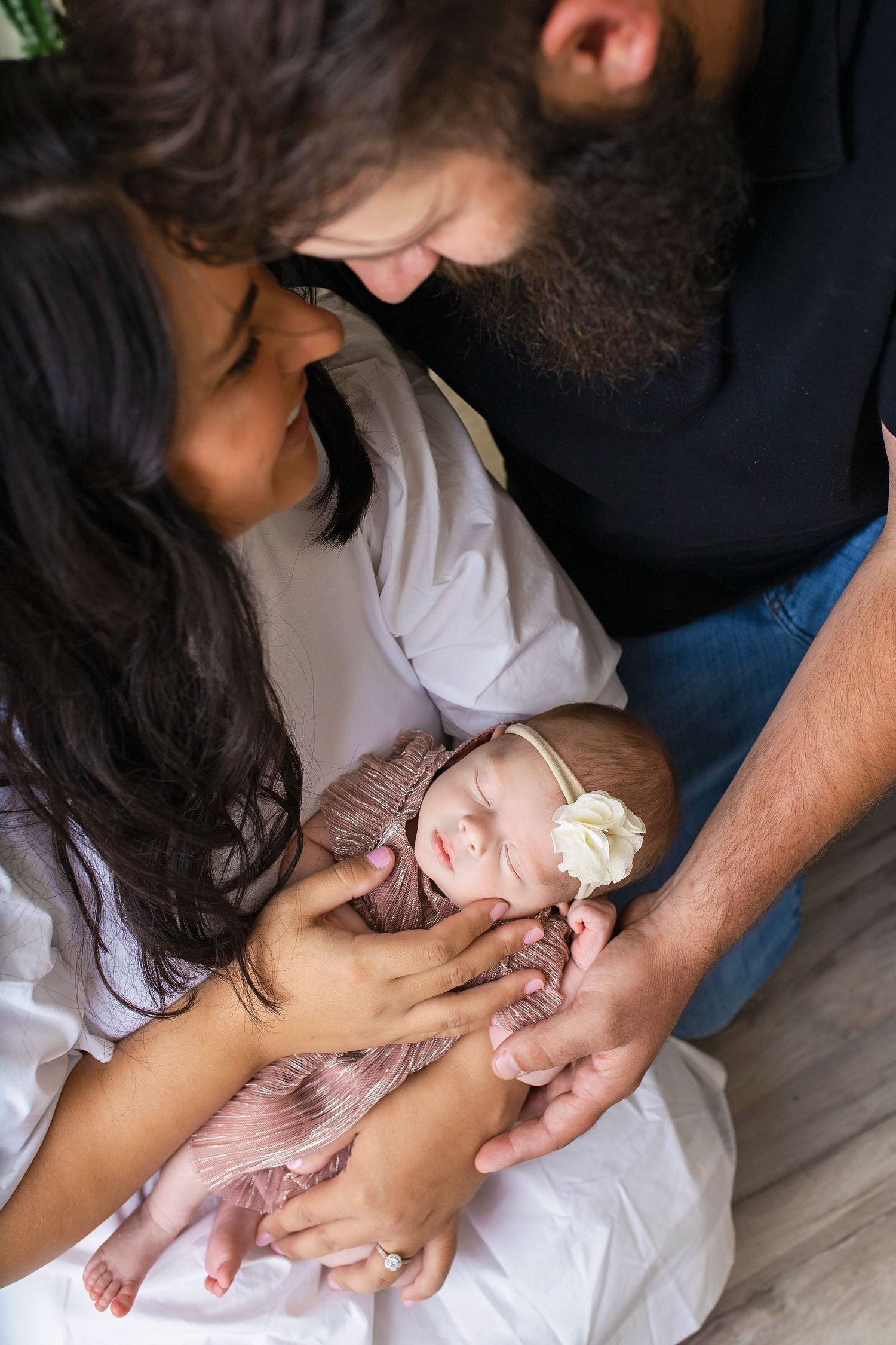 New parents lovingly gazing at their sleeping newborn baby girl wrapped in pink swaddle cloth.