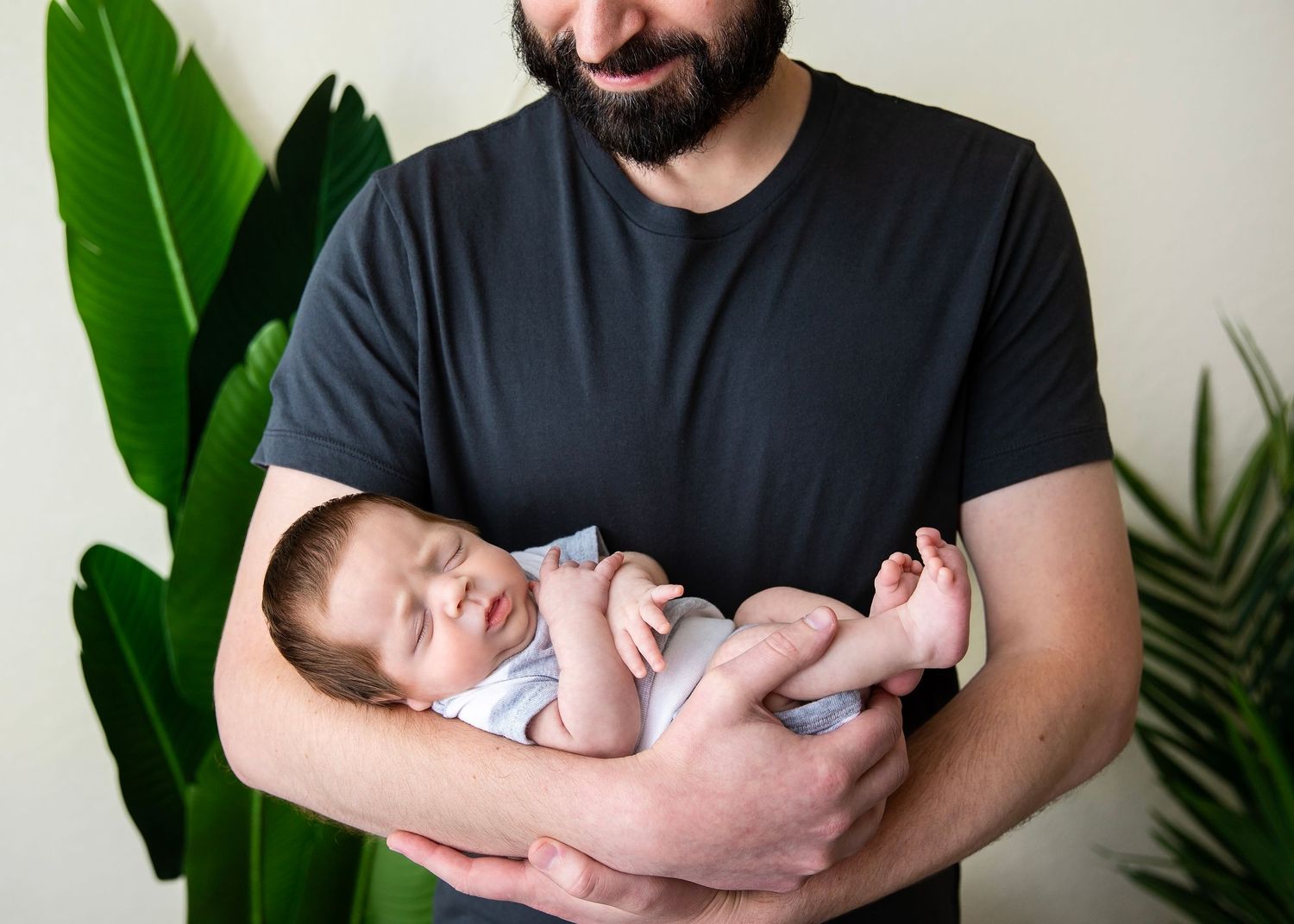 Bearded father cradling his sleeping newborn baby in his arms indoors.