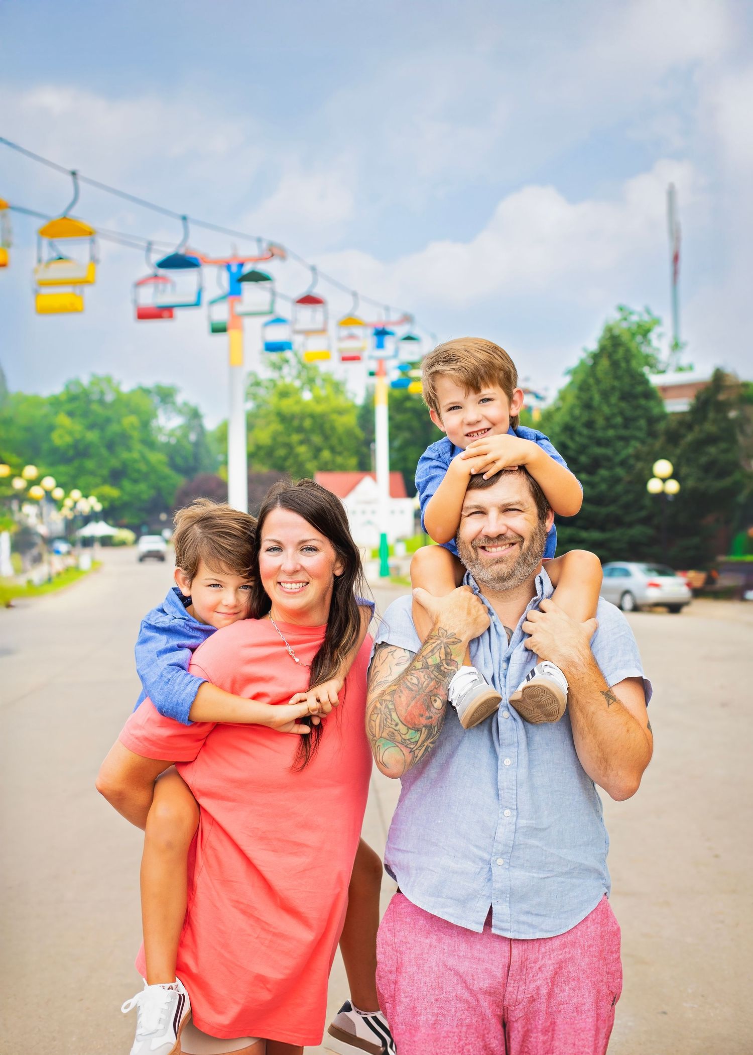 Joyful family posing together at an amusement park with colorful cable cars in the background.