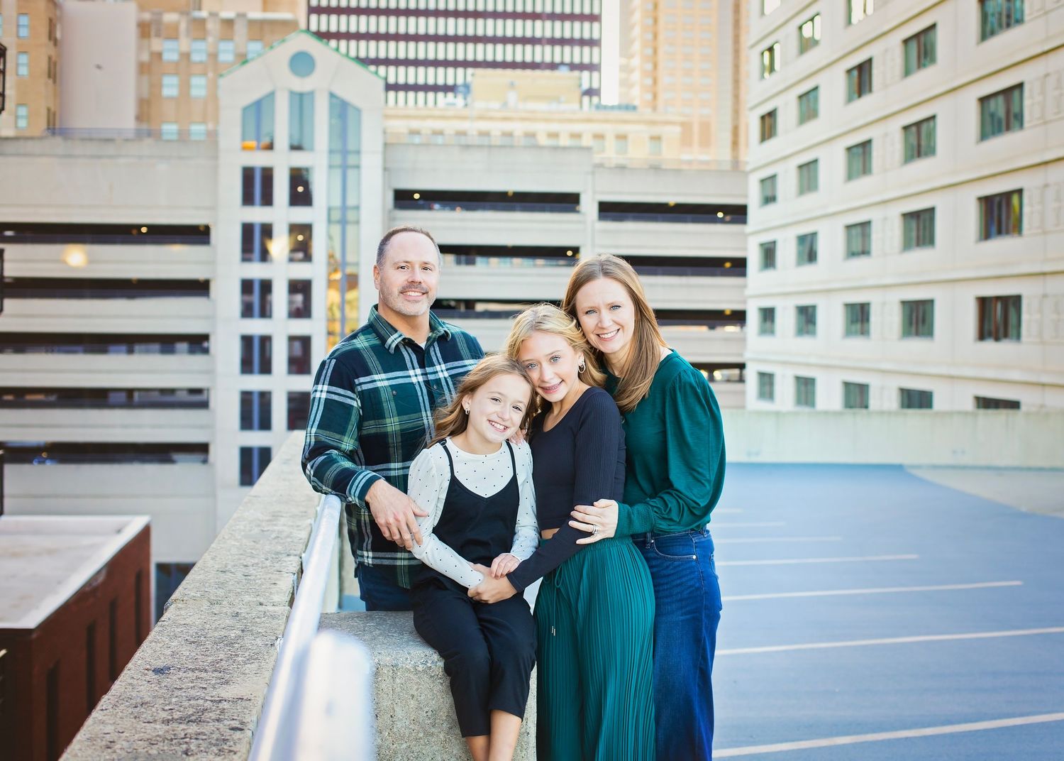Family of four smiling together on a rooftop with city buildings in background.