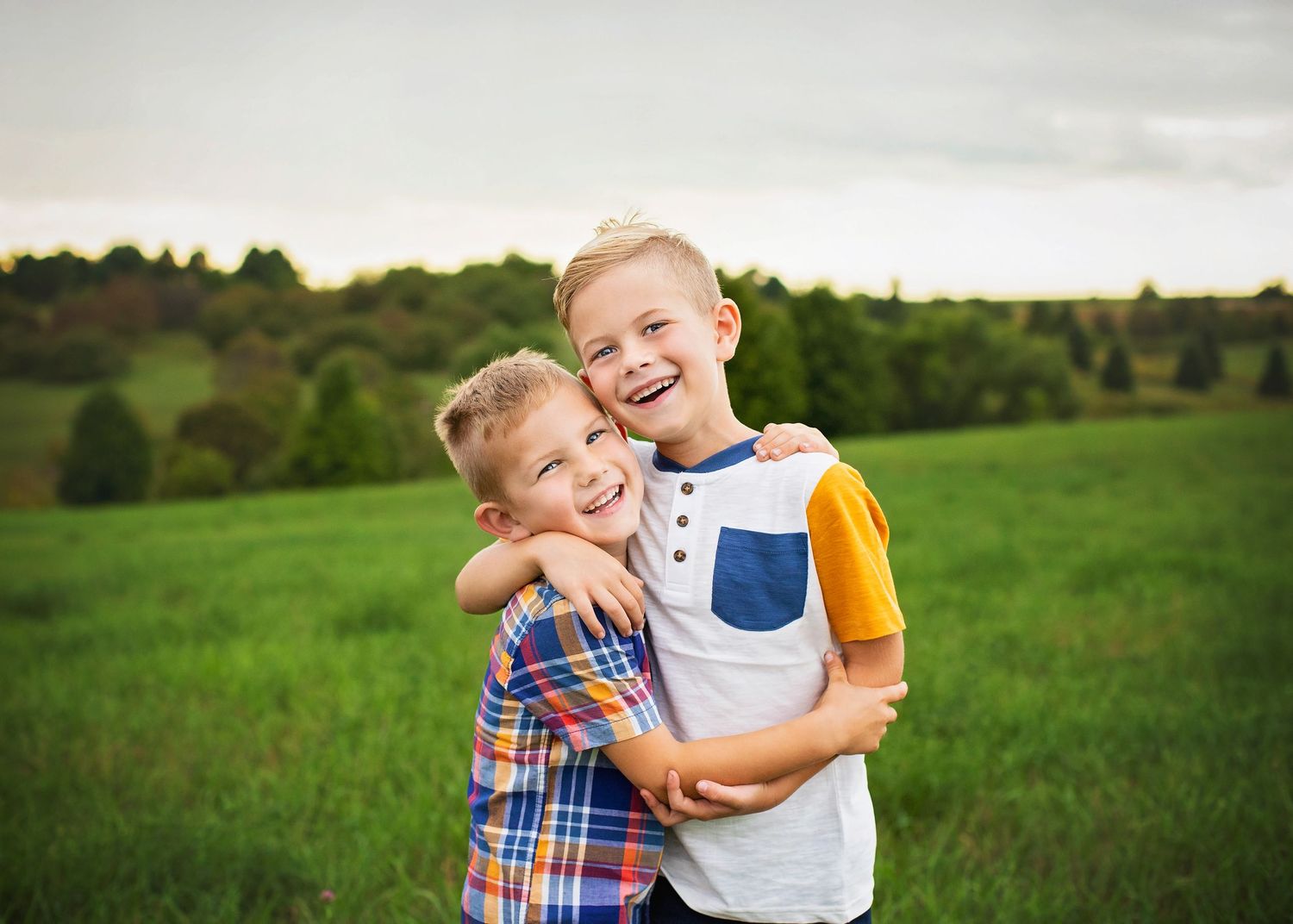 Two young brothers hugging and laughing together in a lush green field at sunset.