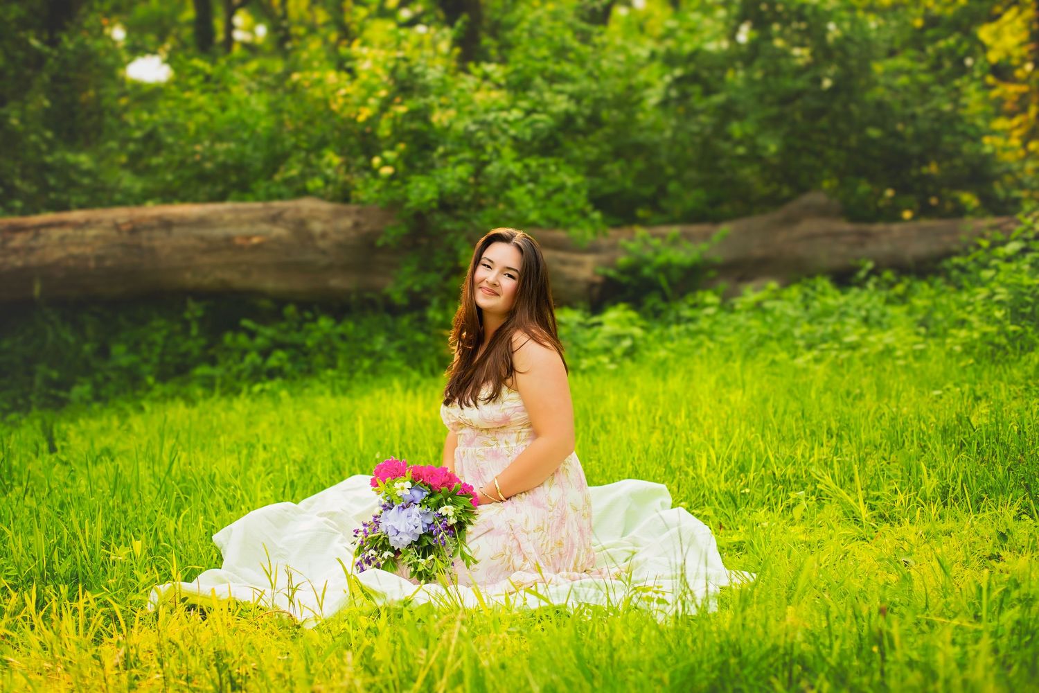Young woman in lace dress sitting on grass holding colorful bouquet in park.
