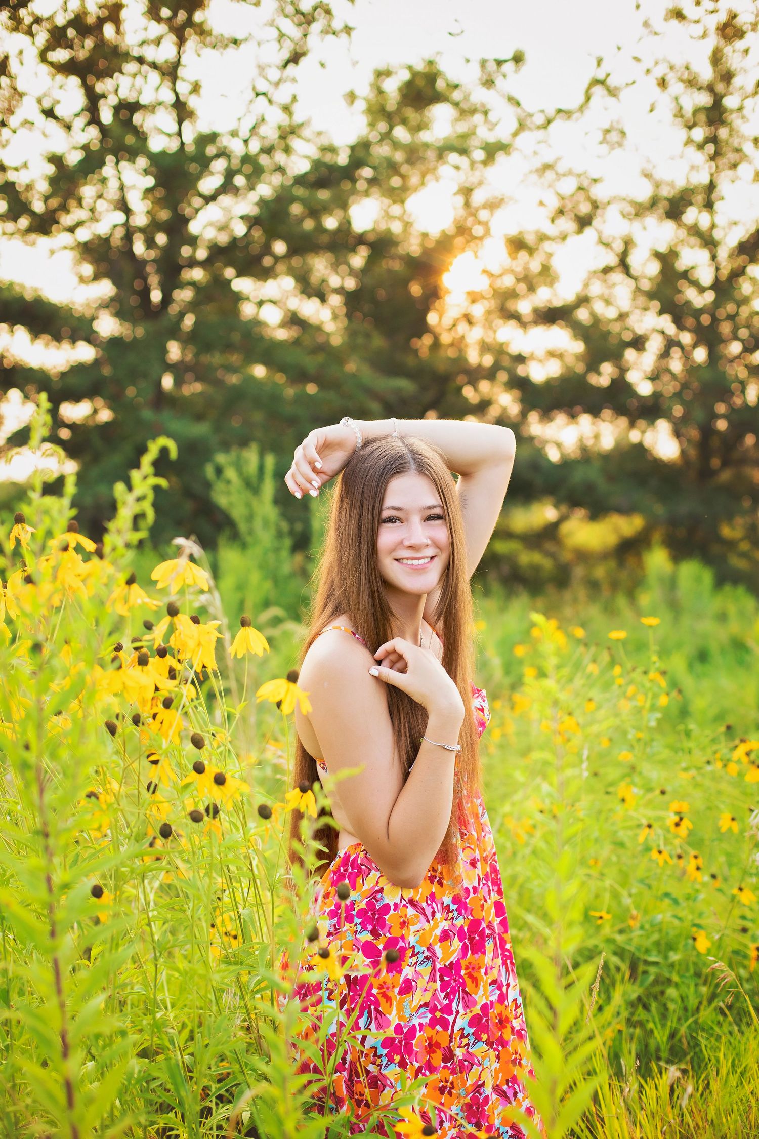 Happy teenage girl in floral dress standing among wildflowers in golden sunset light outdoors.