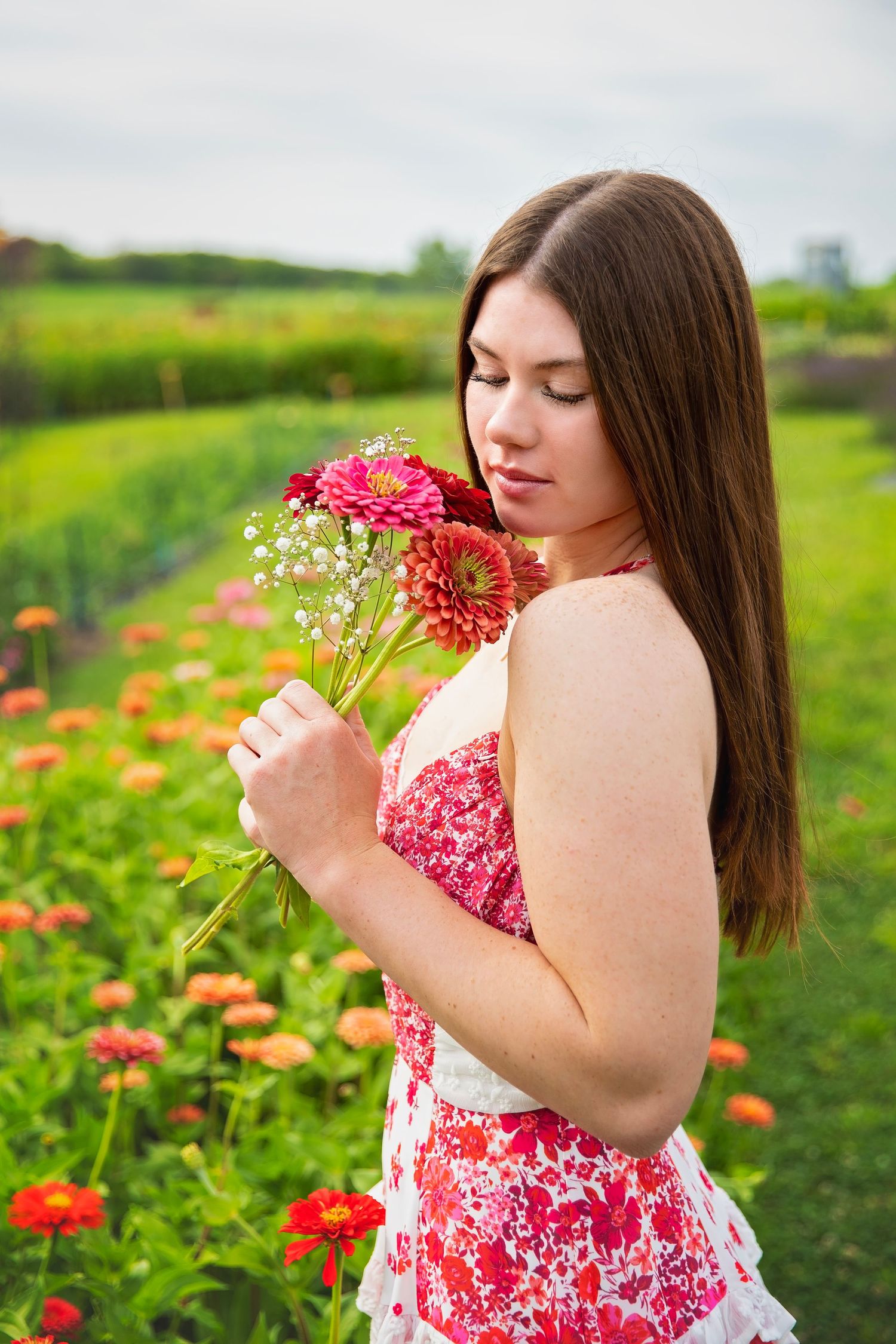 Teen girl smelling red flowers in colorful garden field.
