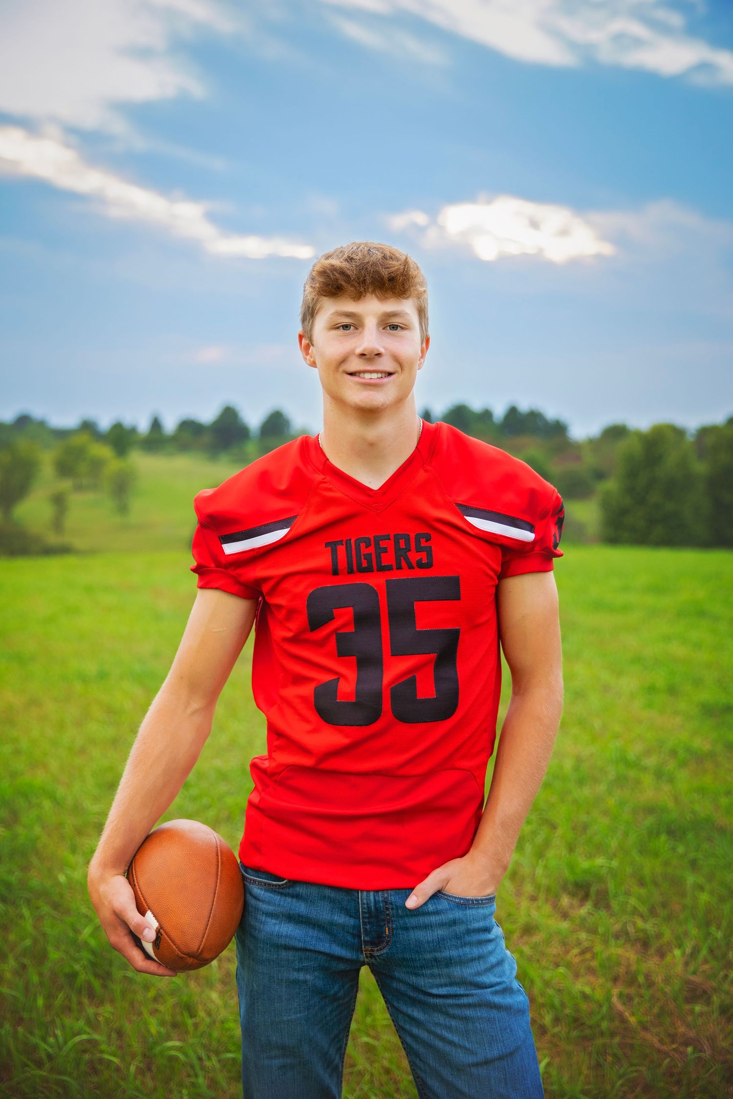 Teen football player in red Tigers jersey number 35 holding a football in a green field.